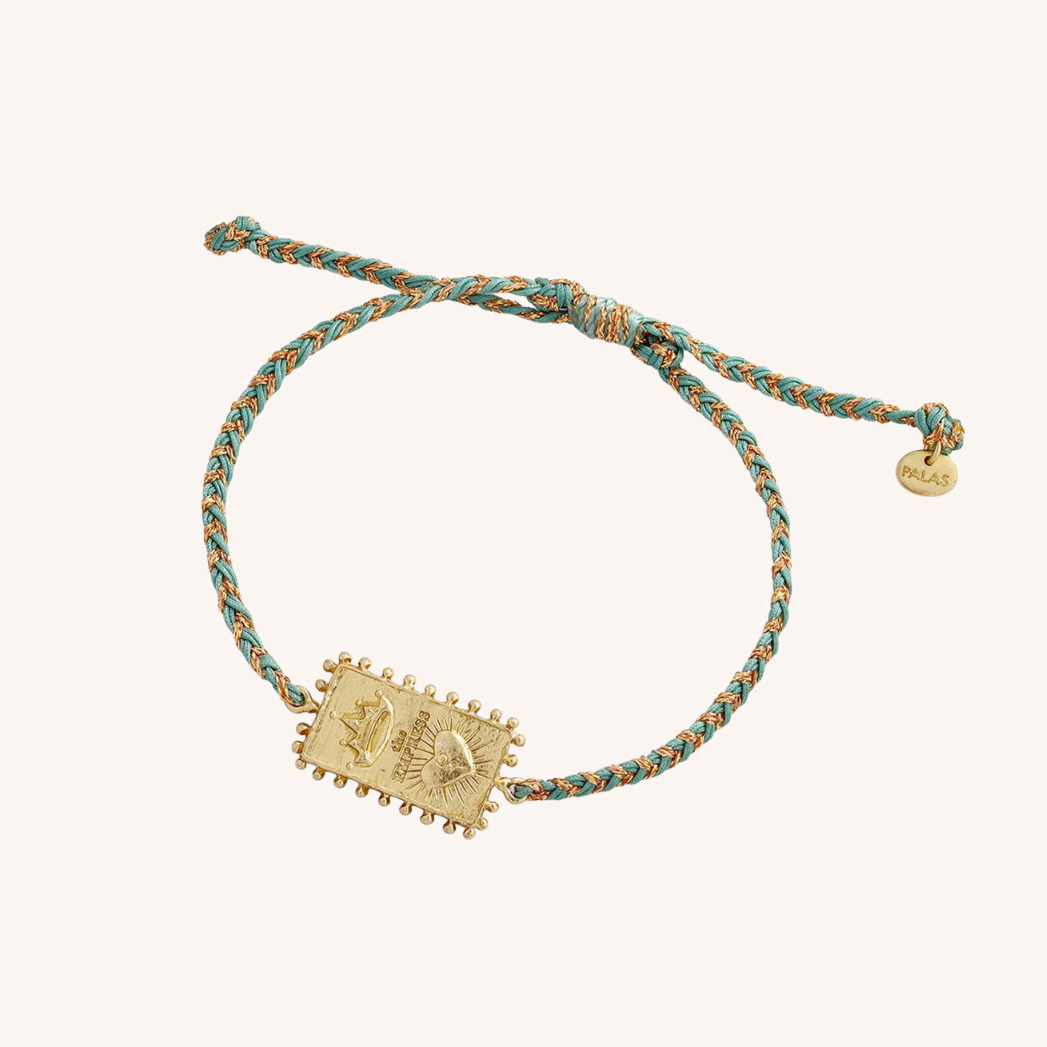 Bracelet with gold charm and braided light green cord on a cream background