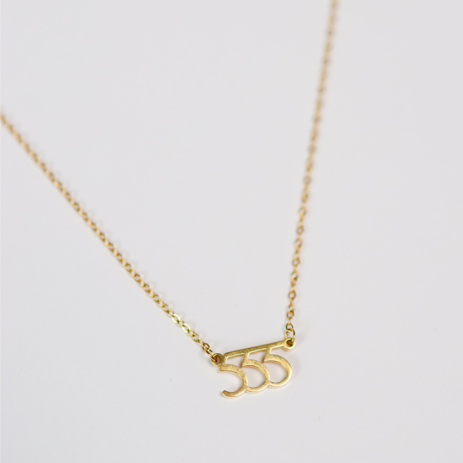 Gold necklace with a '555' pendant on a light gray background