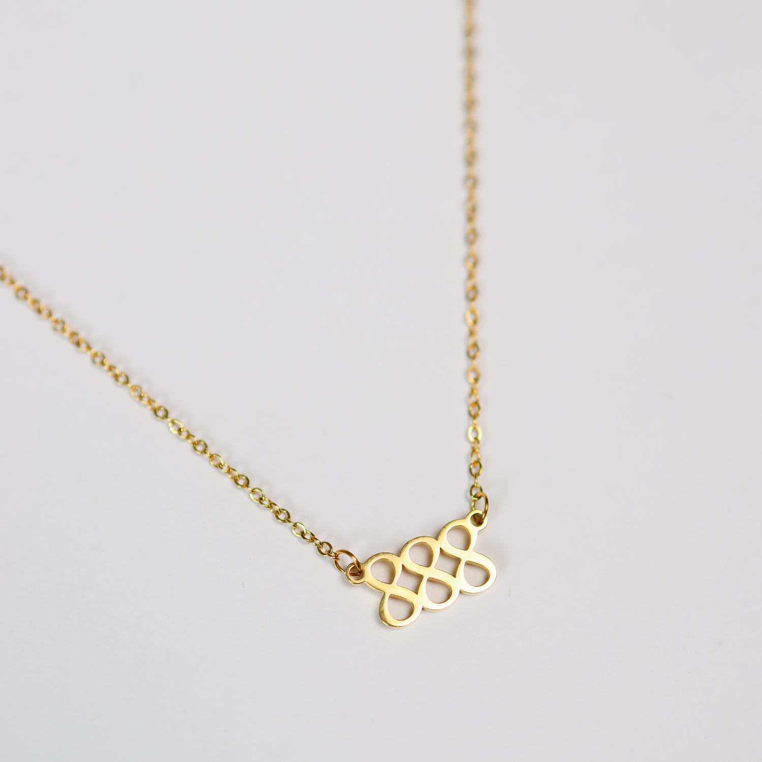 Gold necklace with a triple 8 angel number pendant on a light gray background
