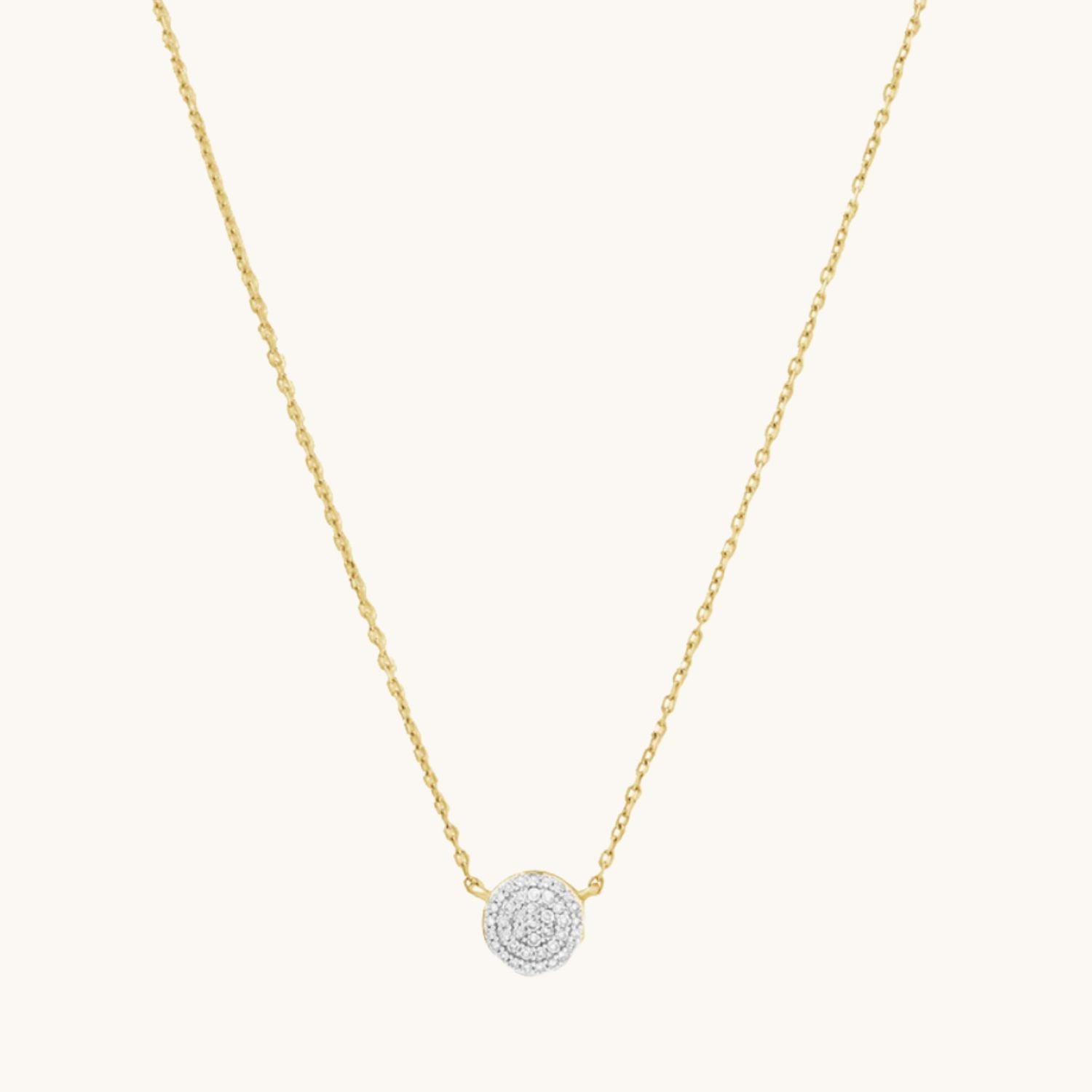 Gold necklace with a round zircon pendant on a cream background