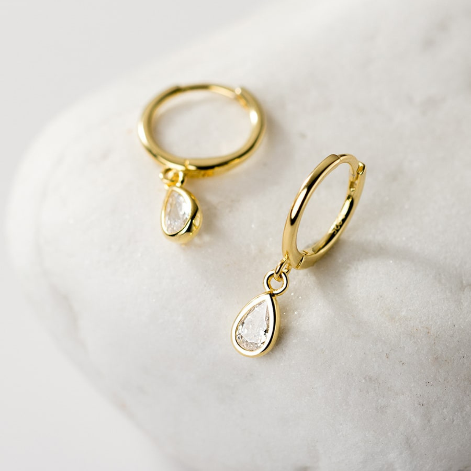 Gold hoop earrings with teardrop-shaped rhinestone on a light marble background