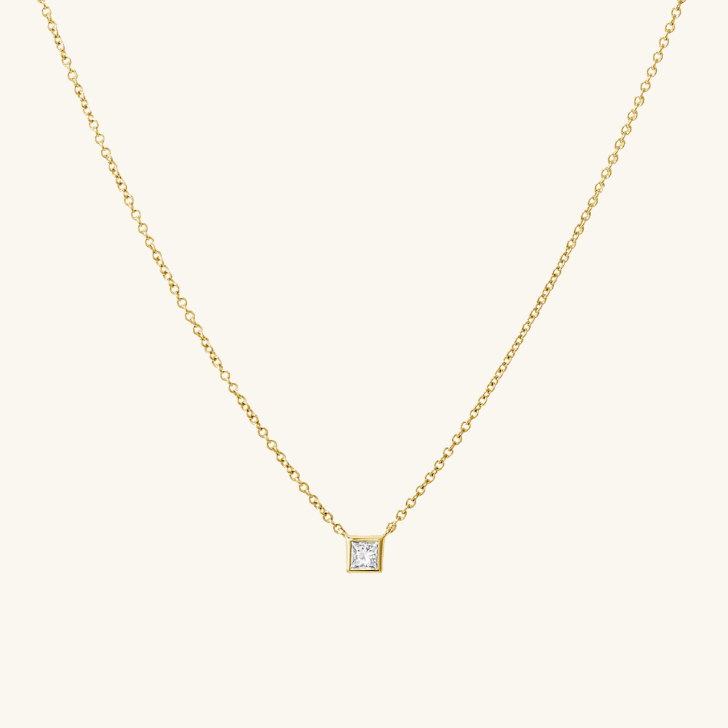 Gold necklace with a square-cut zircon pendant on a light beige background