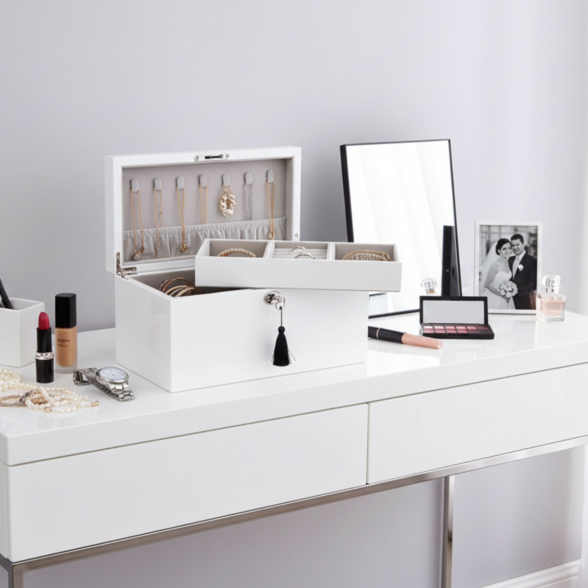 White jewelry box on a vanity with makeup items and a mirror.