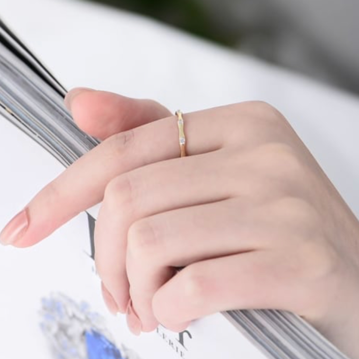 Hand wearing a gold ring on a blurred background