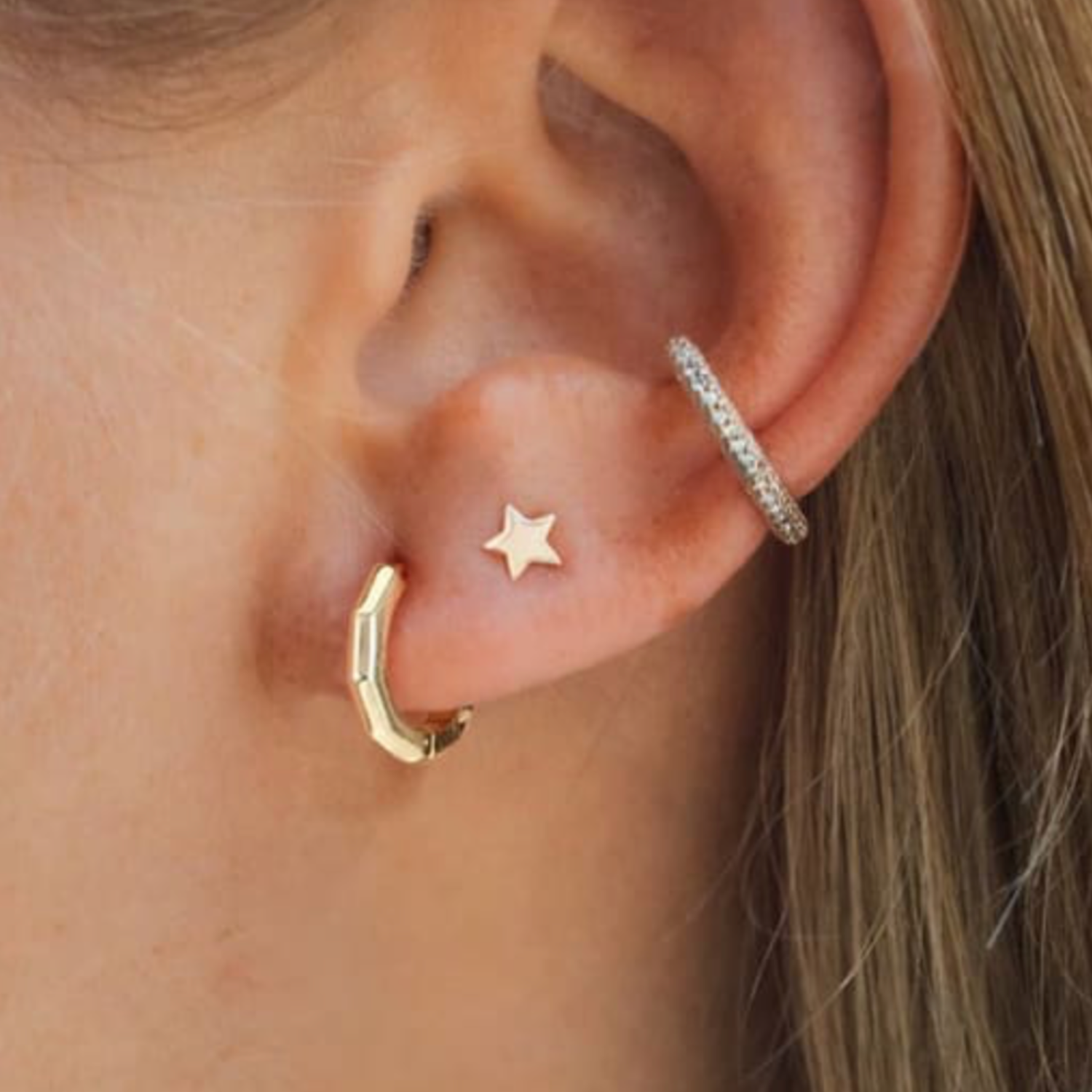 Model wears geometric huggie earring stacked with other earrings