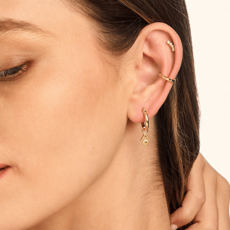 Model wearing Solstice Huggie Earrings, showcasing a gold-plated diamond shaped drop with a sun and star design for an elegant celestial touch