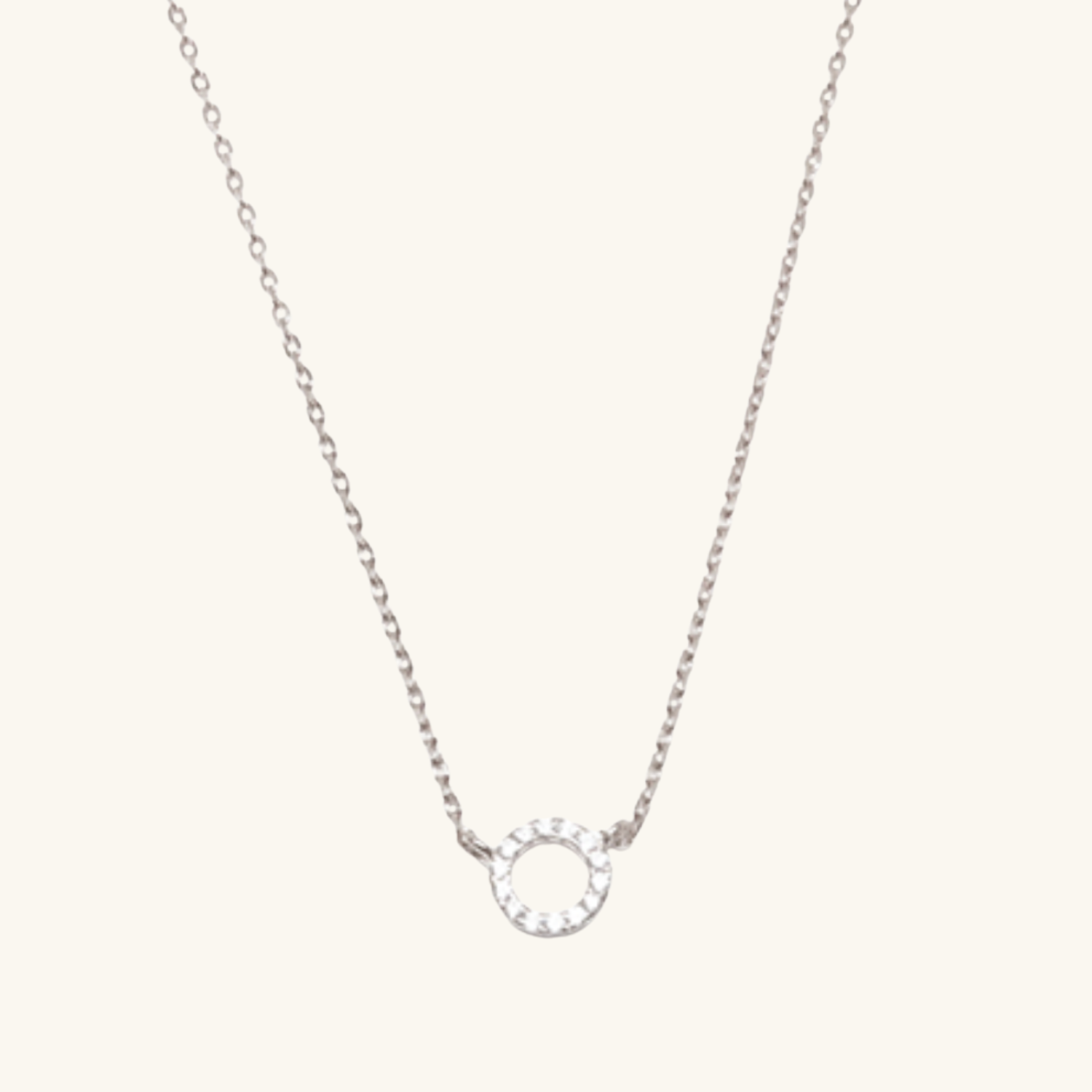 Silver necklace with a small circular pendant on a light cream background