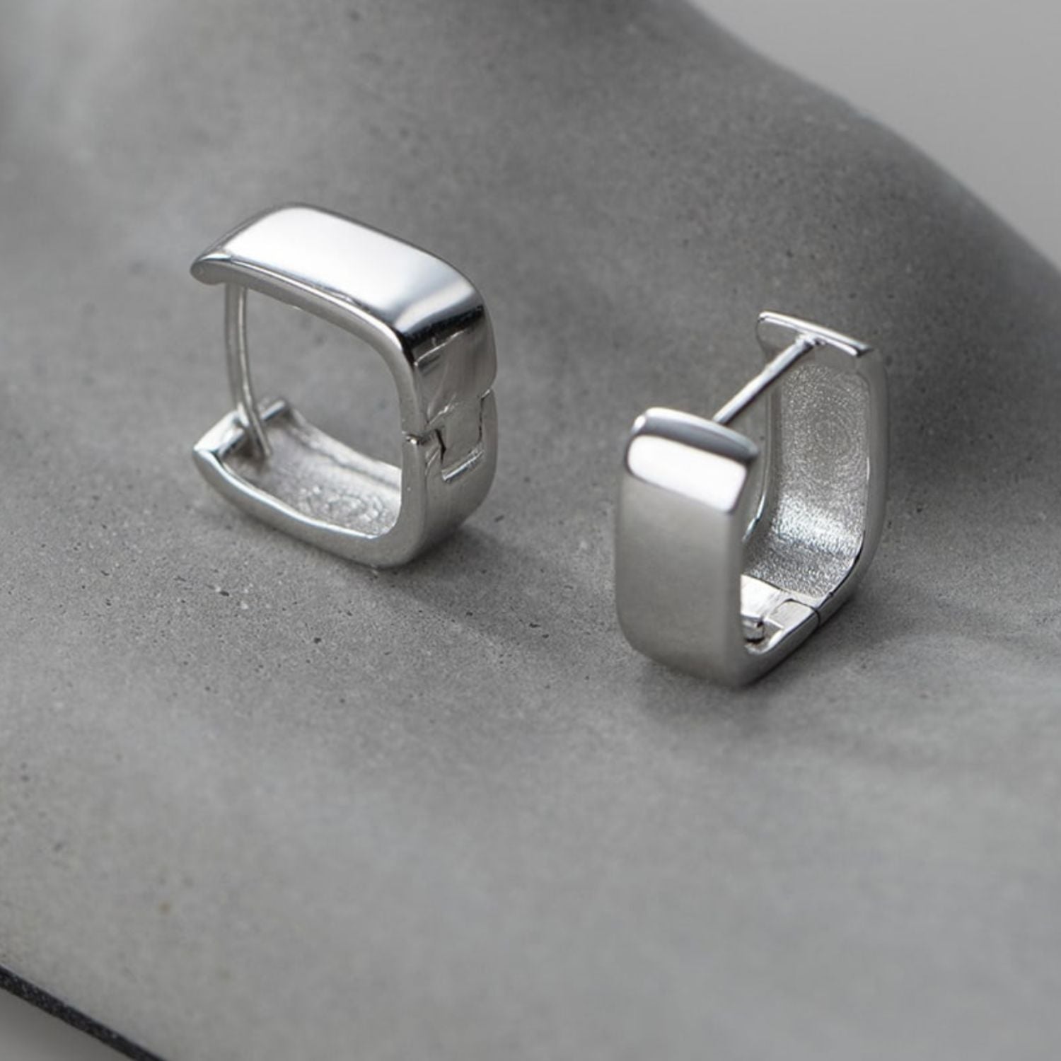Silver icon Huggie earrings in square cube shape, displayed on a grey background for a modern and sleek look