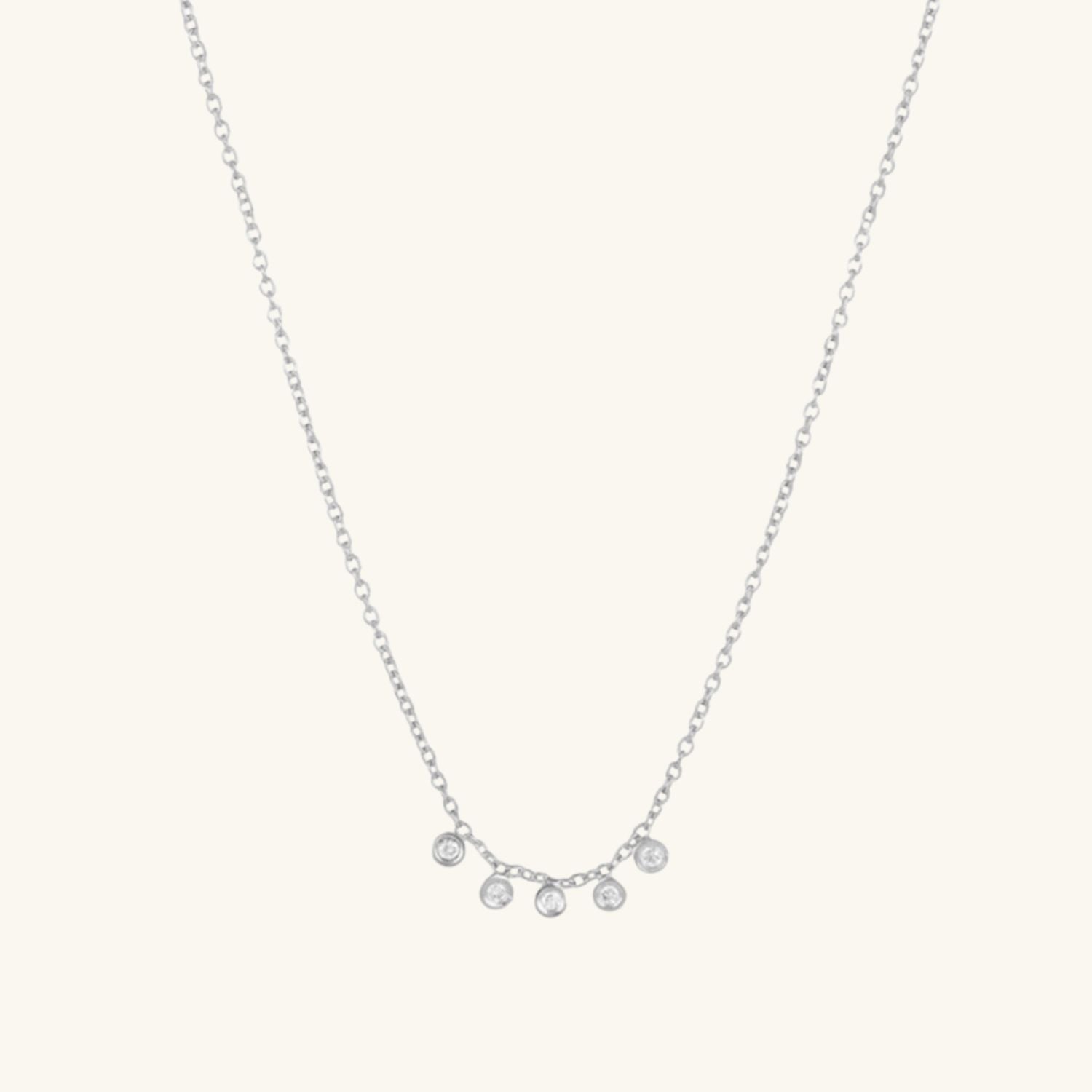 Silver necklace with five small round zircon drops on a cream background