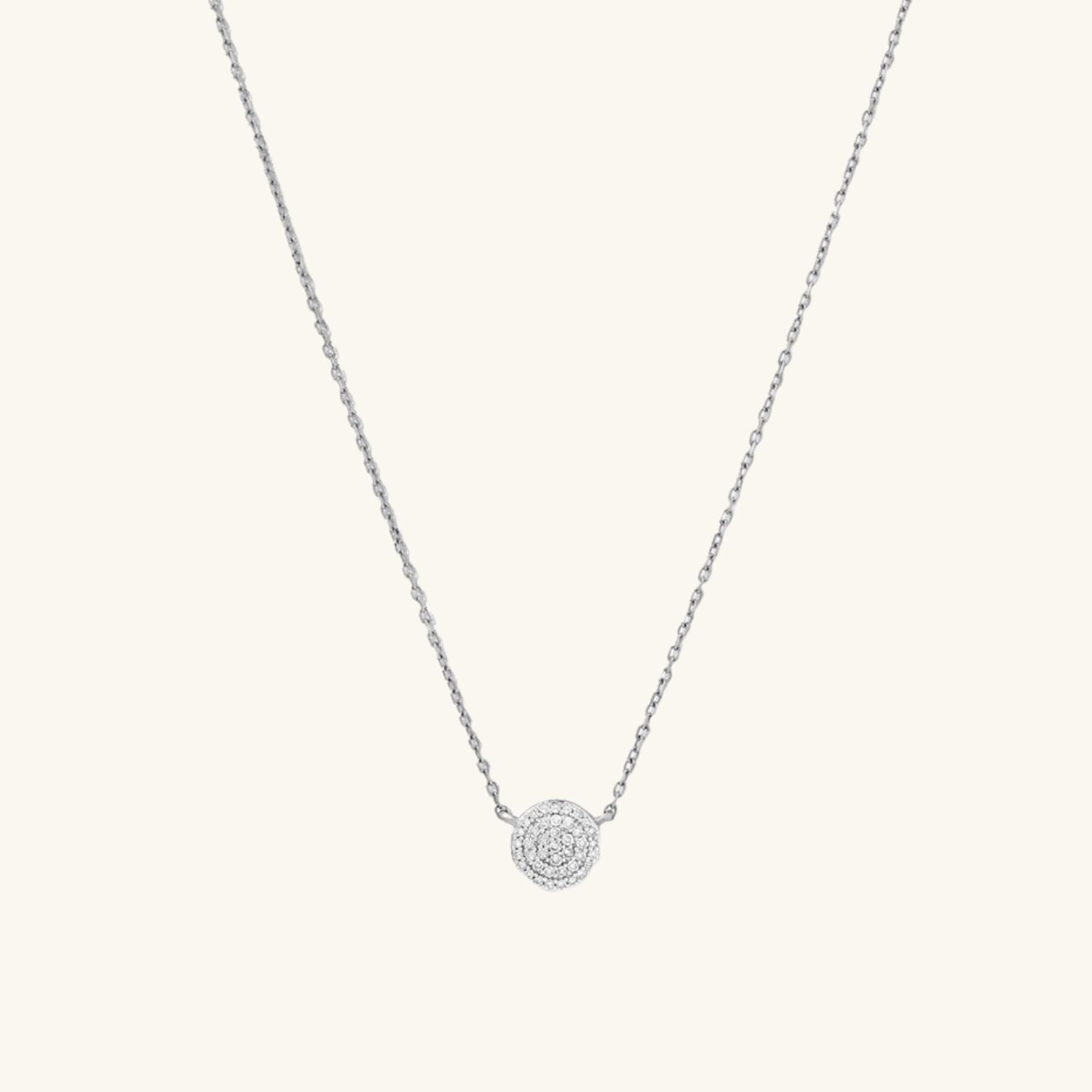 Silver necklace with a round zircon pendant on a light cream background