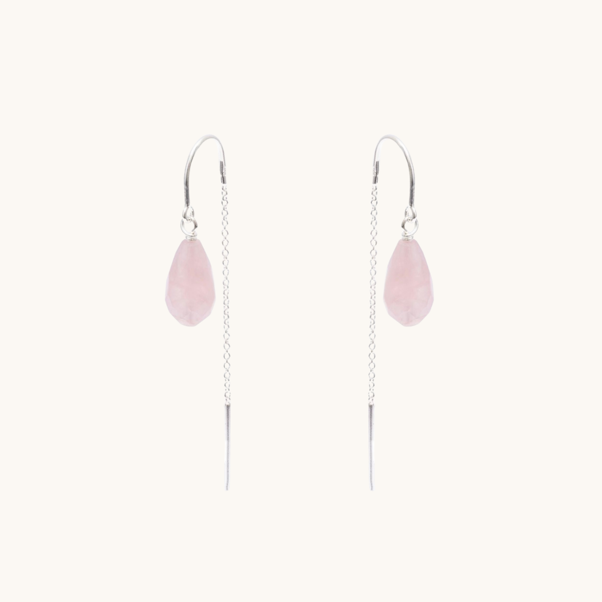 A pair of long dangle earrings featuring a light pink teardrop-shaped stone suspended from a silver wire chain with a silver hook back, set against a solid off-white background.