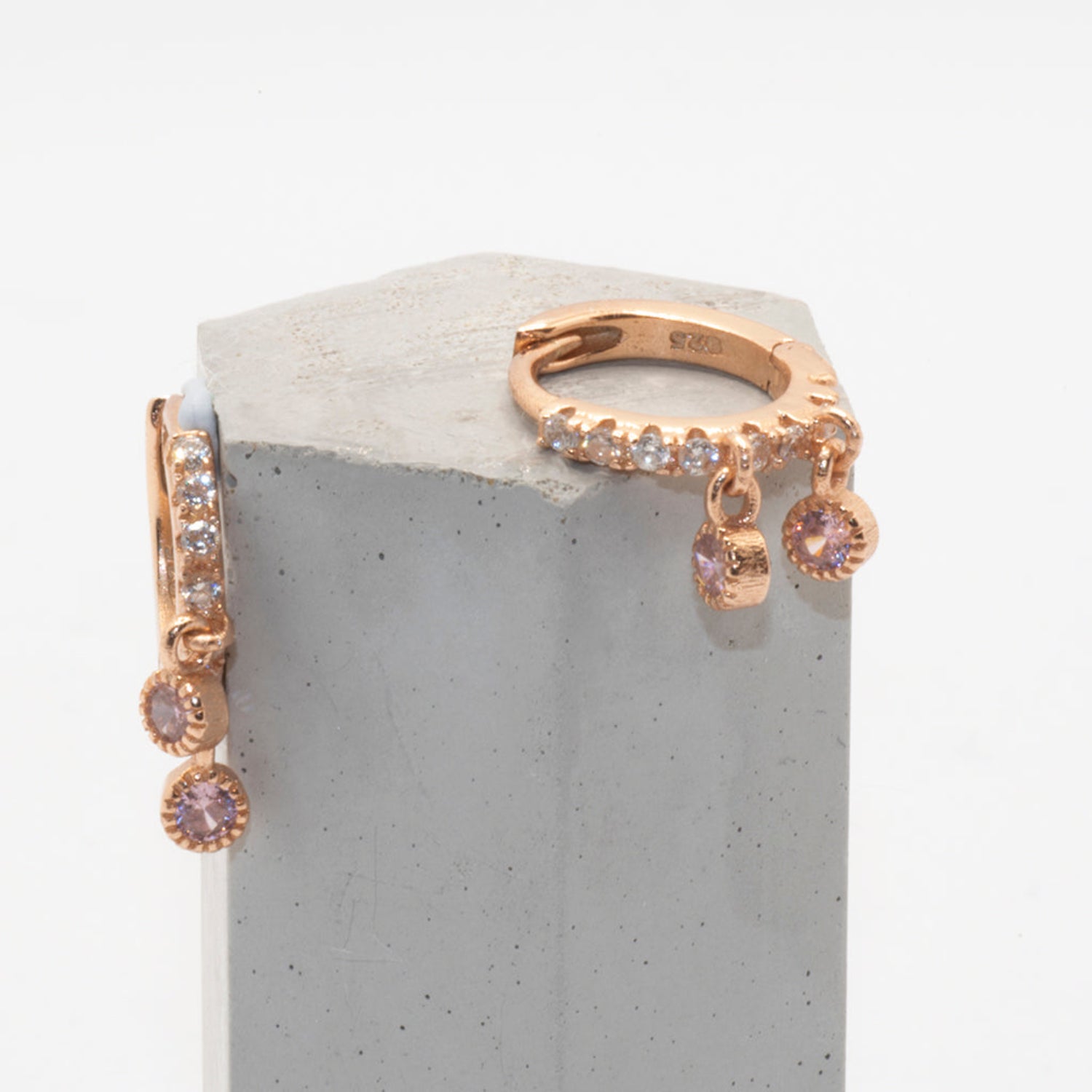 Rose gold huggy earrings with cubic zirconia displayed on small grey column