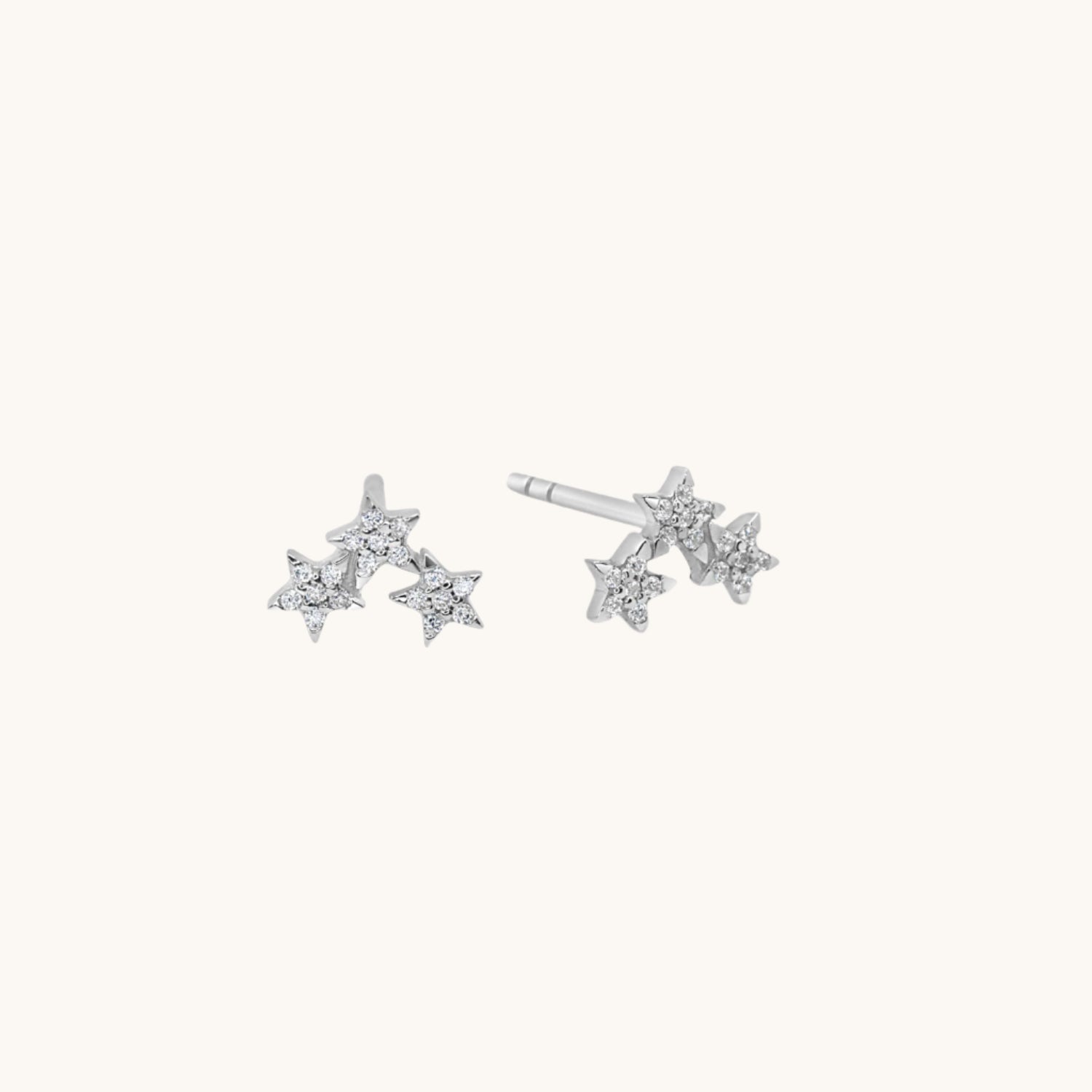 Small silver star cluster earrings shown on warm cream background