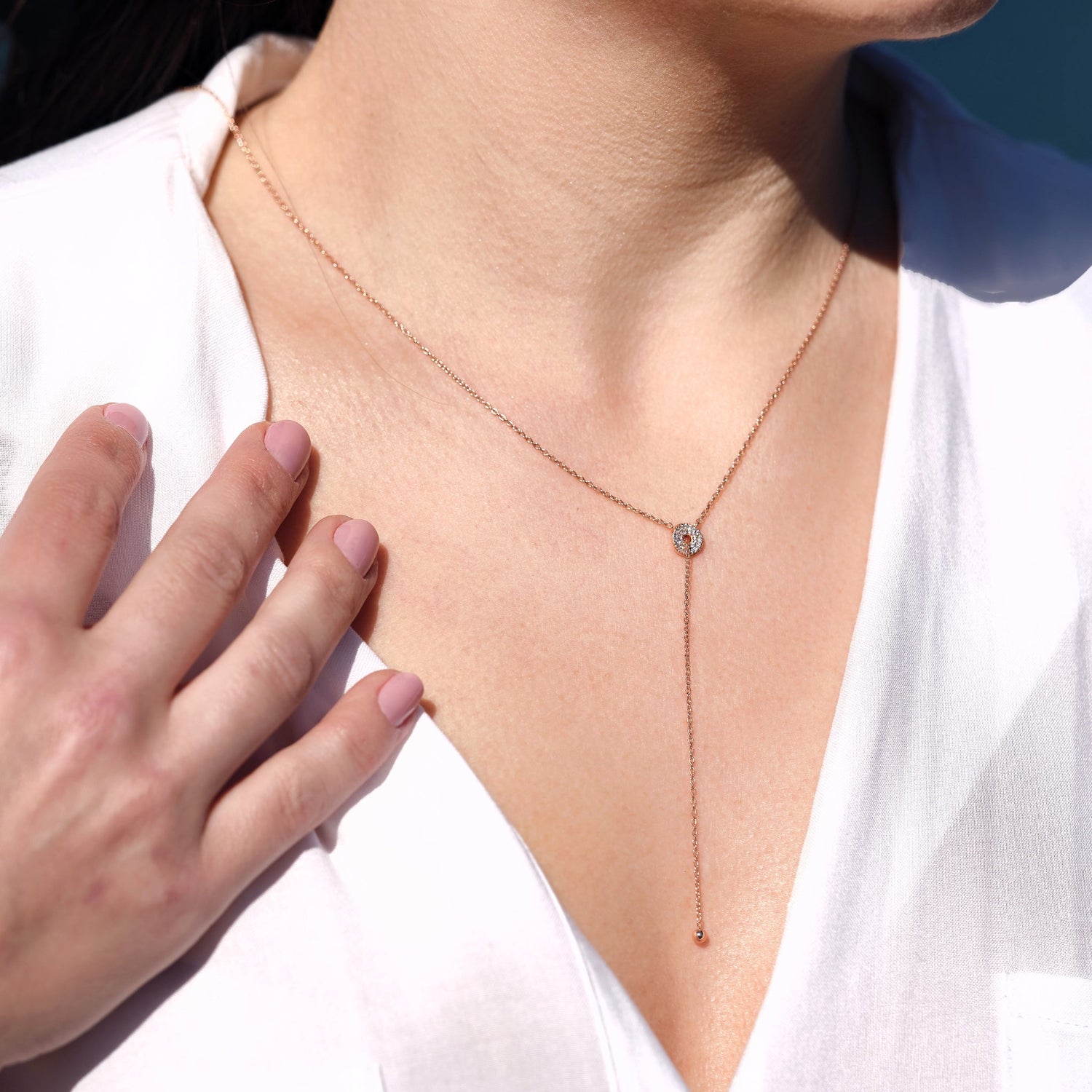 Model wearing Lariat necklace in gold, sitting on neckline with white blouse