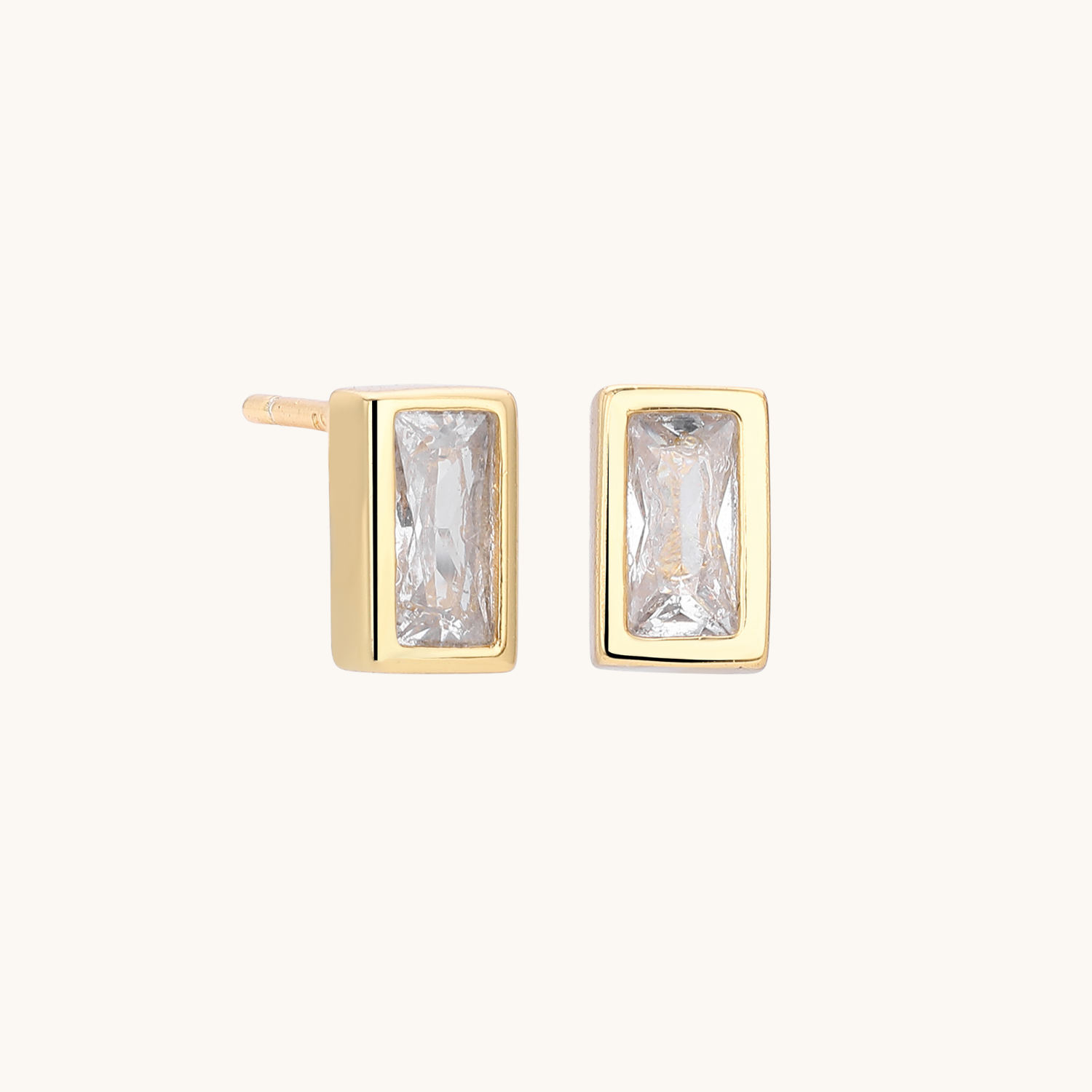 A pair of gold rectangular stud earrings with clear baguette-cut gemstones, shown on a plain off-white background.