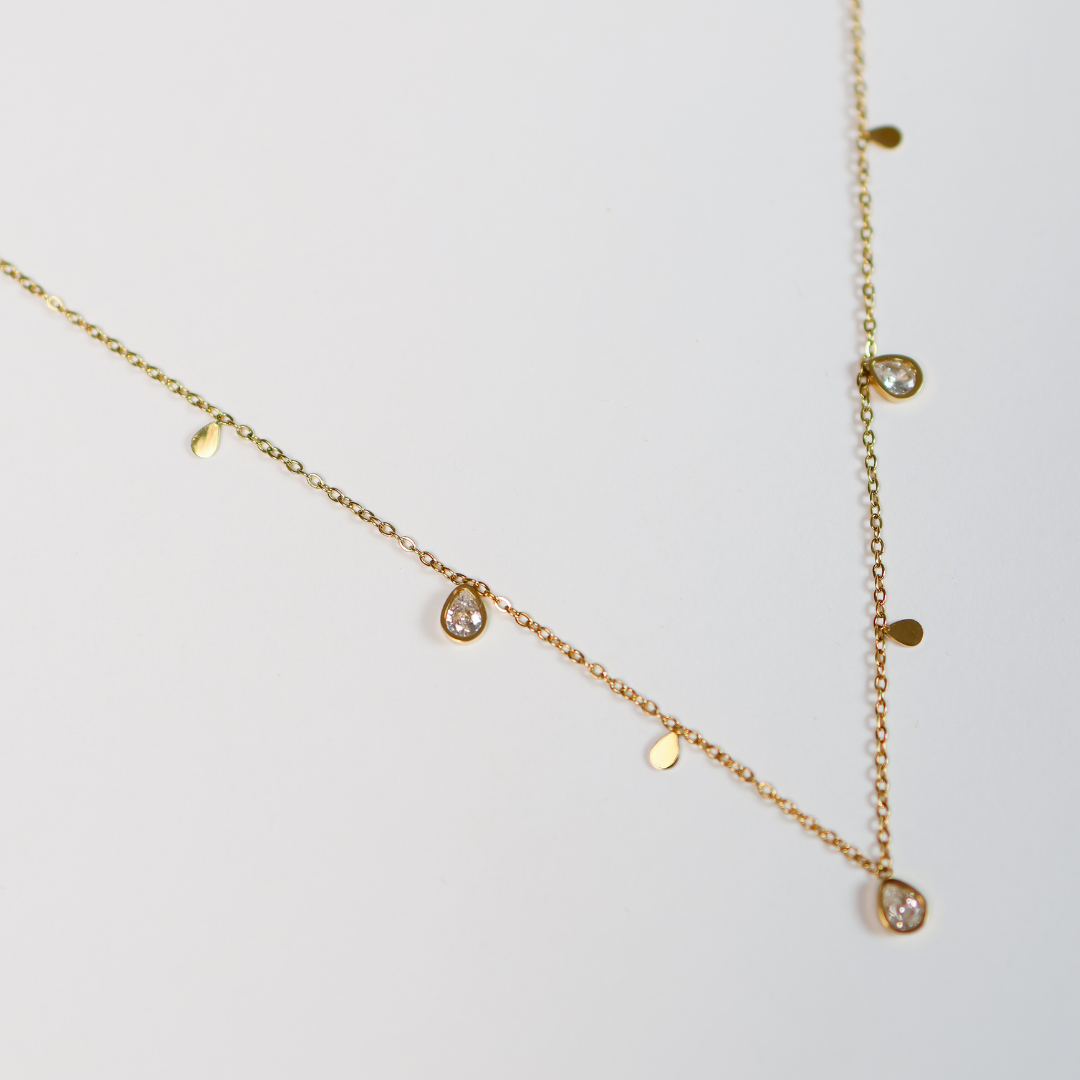 Gold necklace with small diamond-like pendants on a light gray background