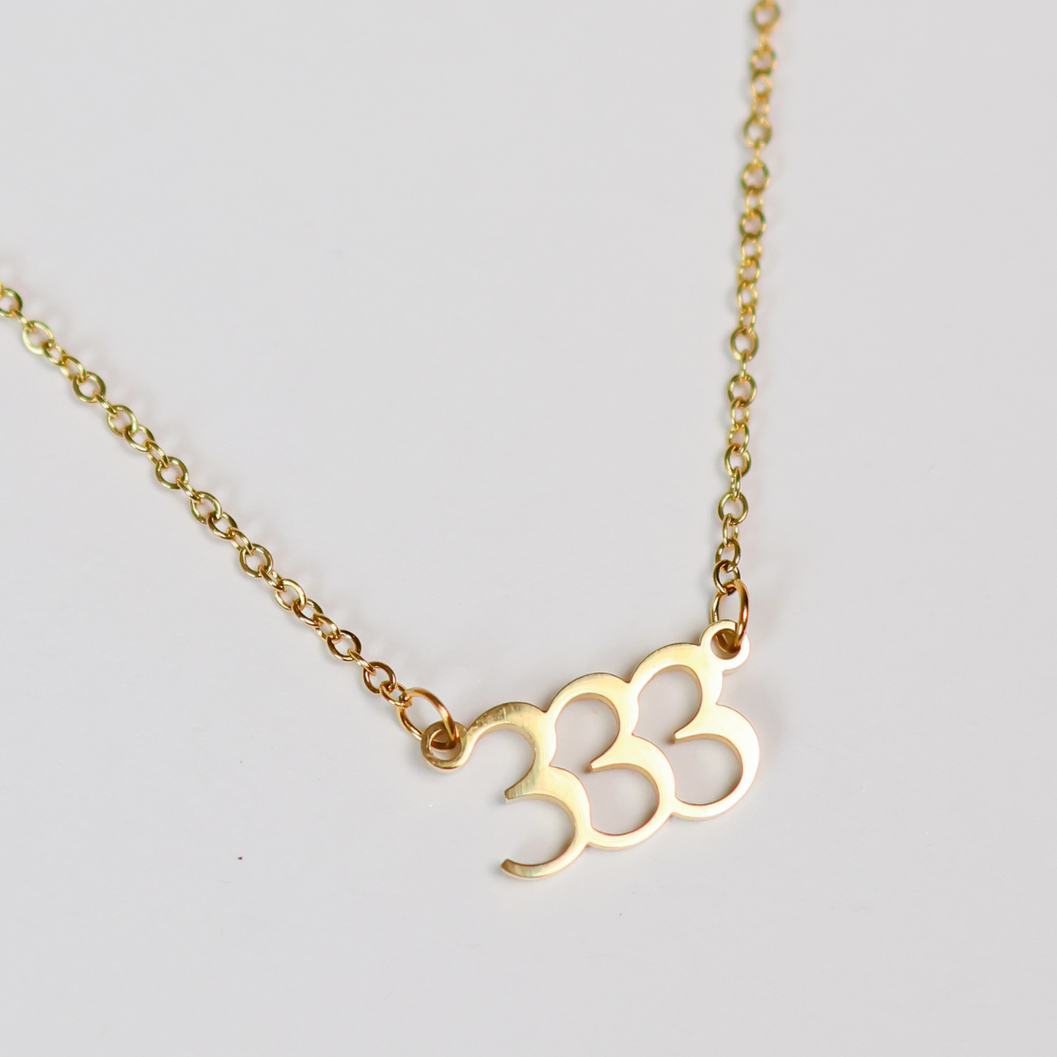 Gold necklace with a '3' pendant on a light gray background