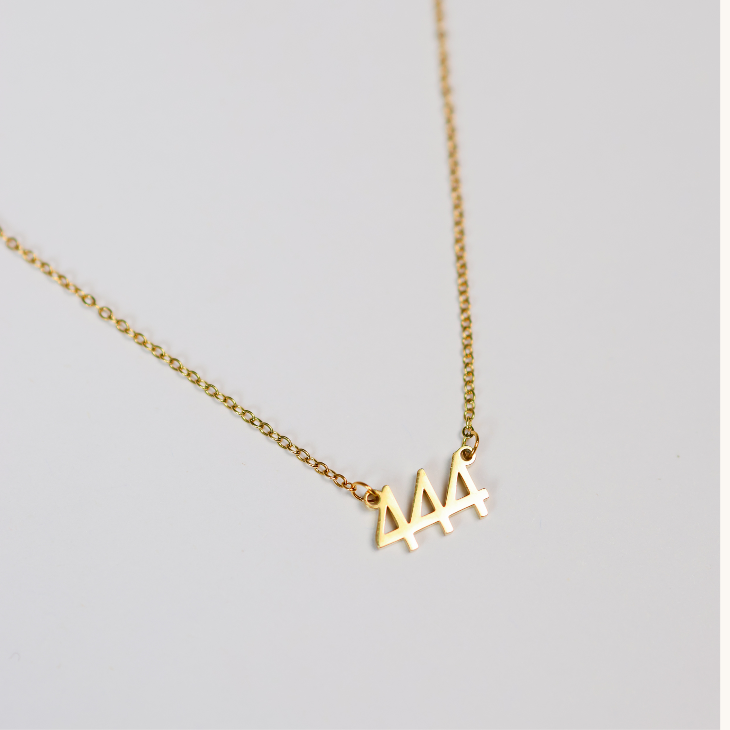Gold necklace with a small triple four pendant on a light gray background