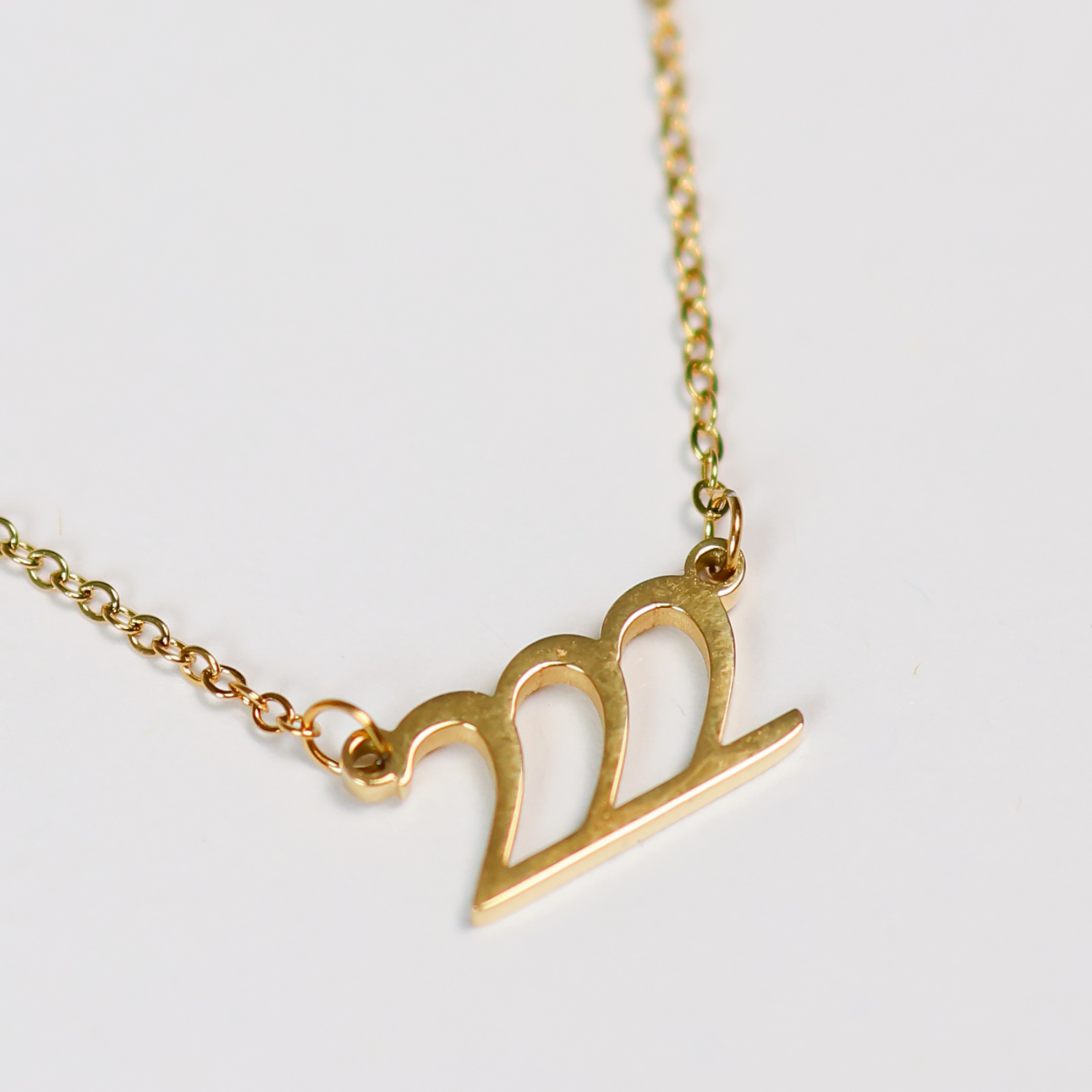 Gold necklace with a tripe 2 pendant on a light gray background