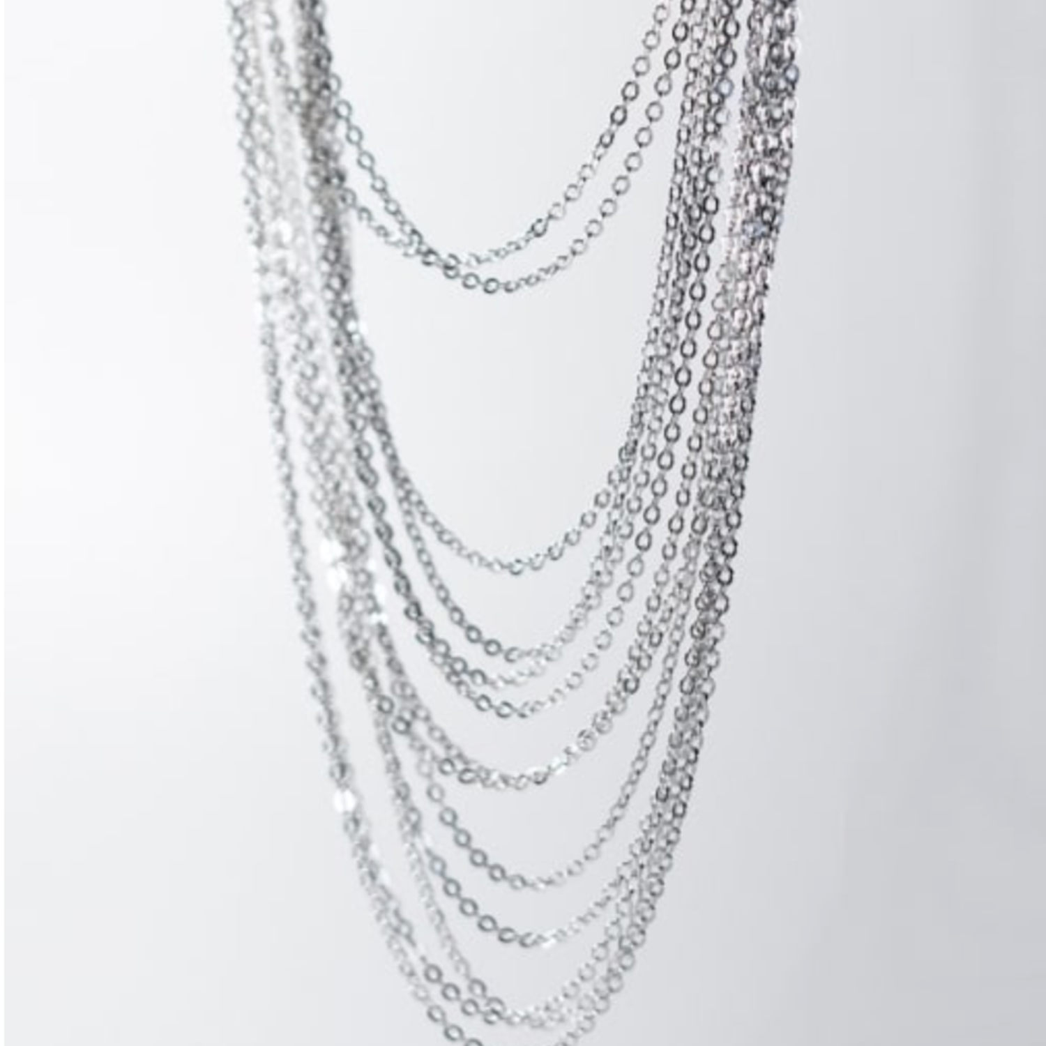 Multiple silver chain necklaces on a light gray background