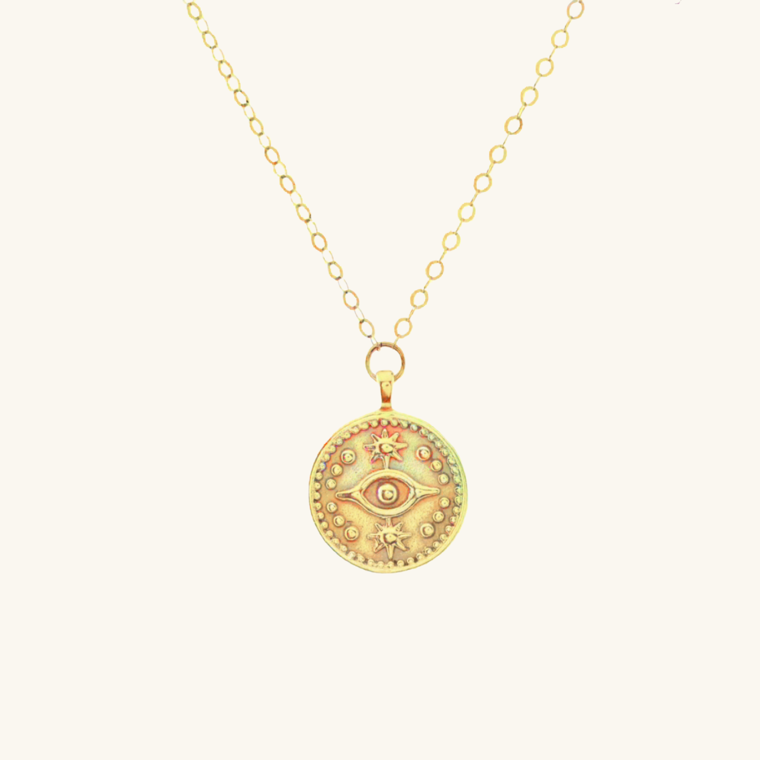 Gold necklace with a decorative evil eye pendant on a light beige background