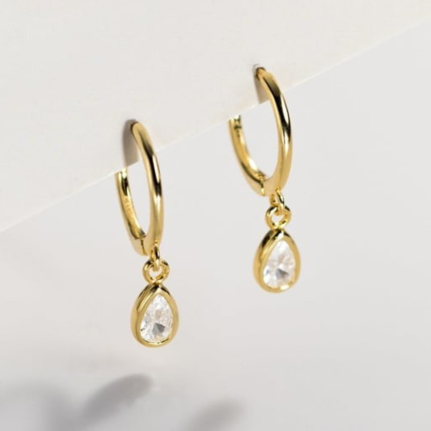 Gold hoop earrings with teardrop-shaped rhinestone on a light gray background