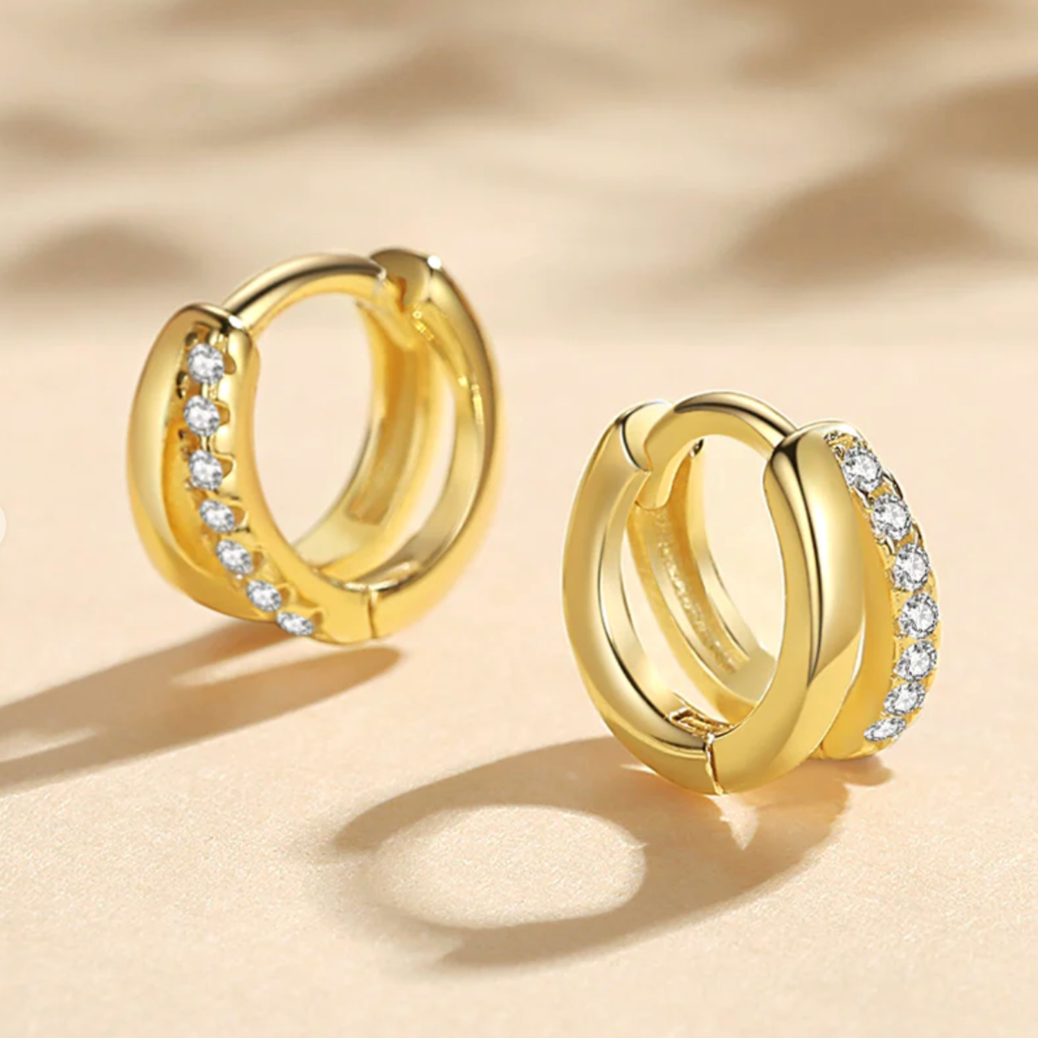 Gold huggie earrings with embedded stones on a beige background