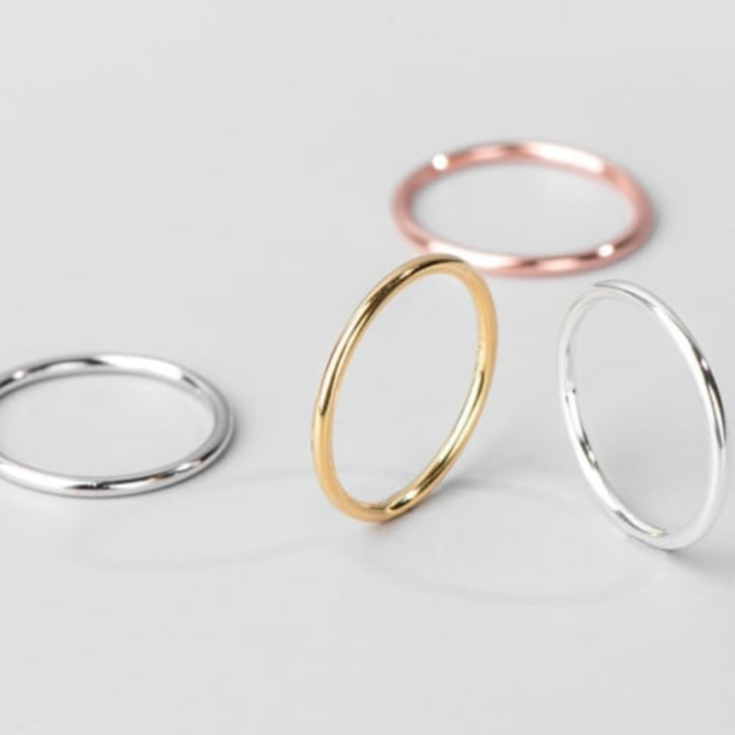 Four thin rings in gold, rose gold, and silver on a light gray background