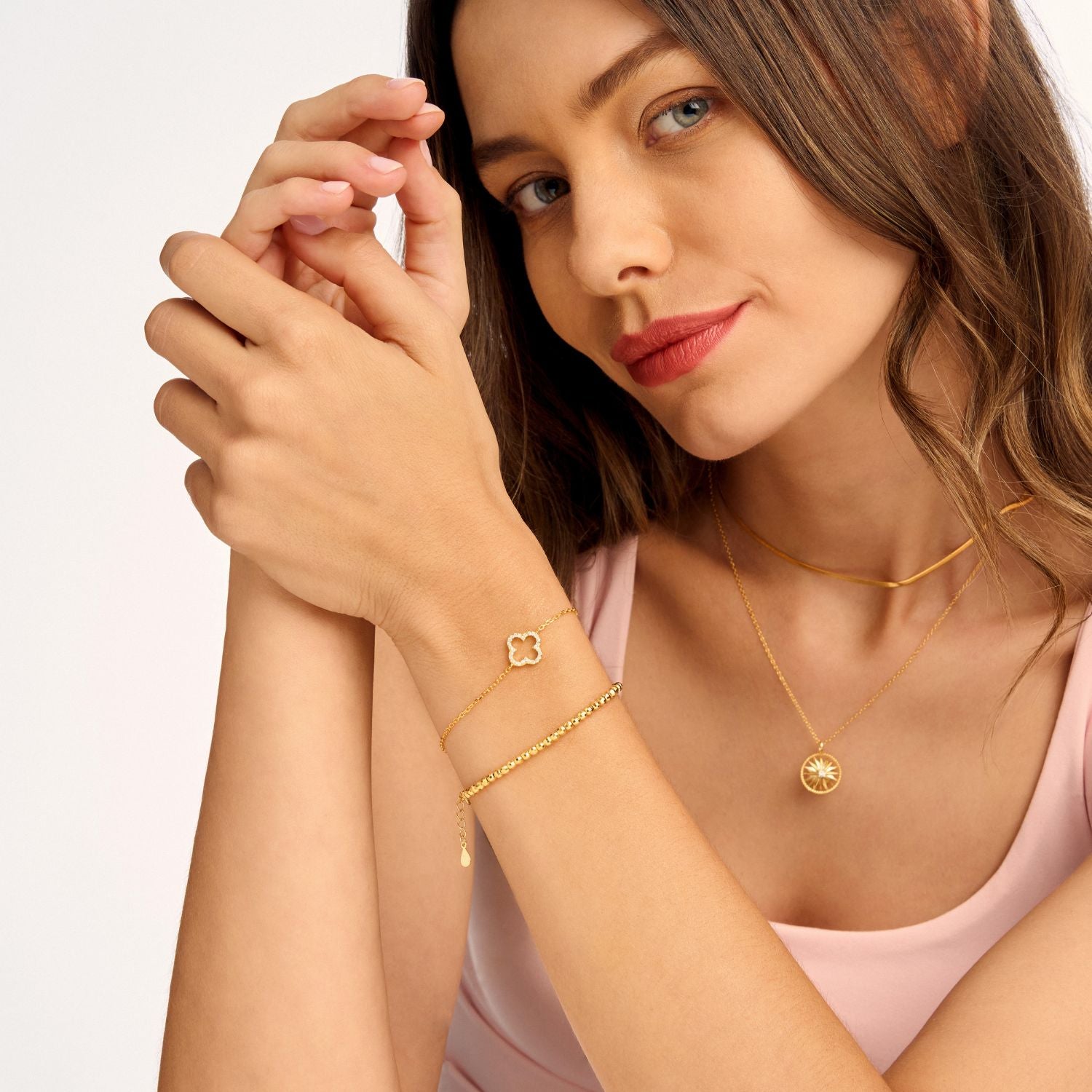 Model wearing gold radiance bracelet stacked with a four leaf clover bracelet, creating a stylish layered look with a touch of luck and elegance