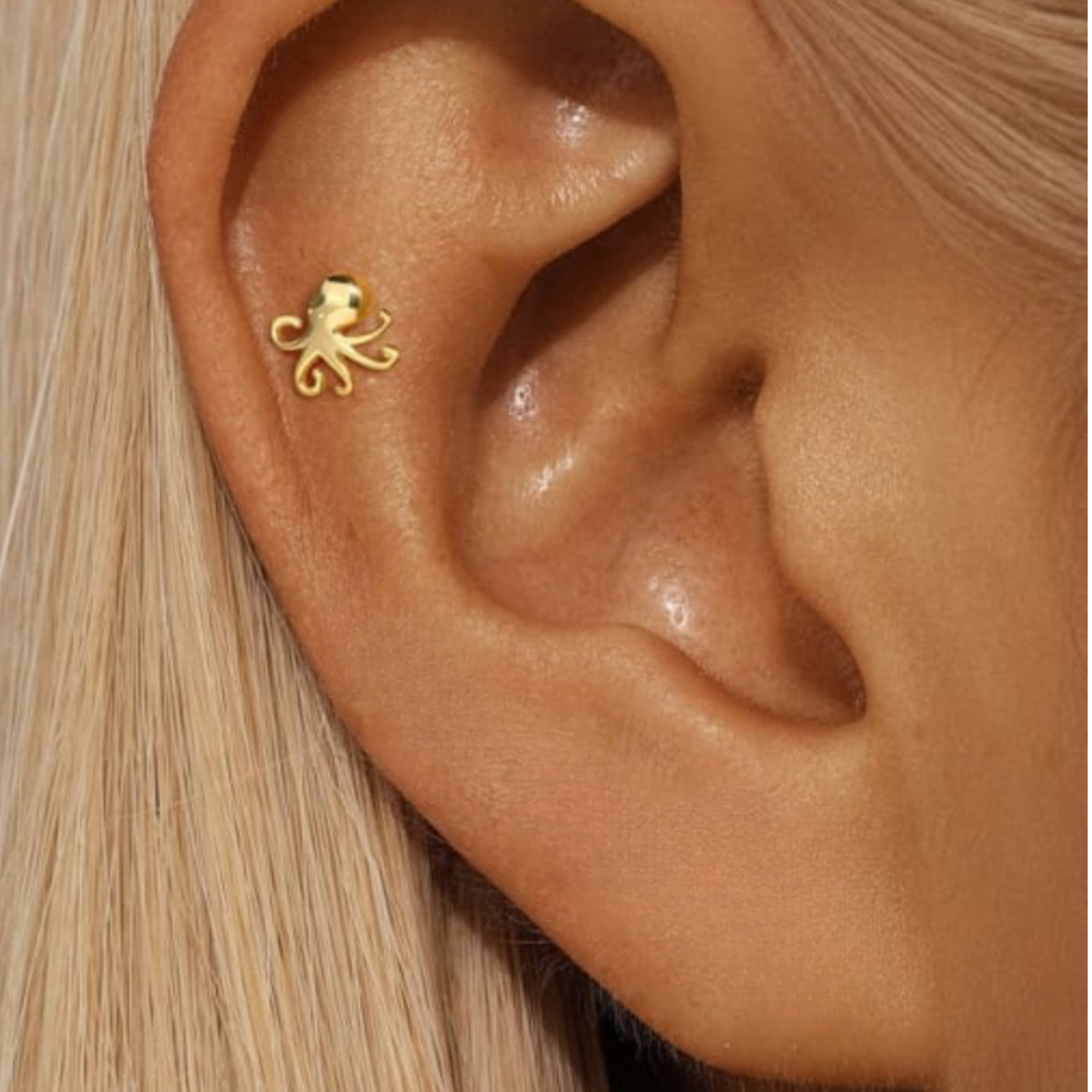 Gold octopus earring on a person's ear with blonde hair.