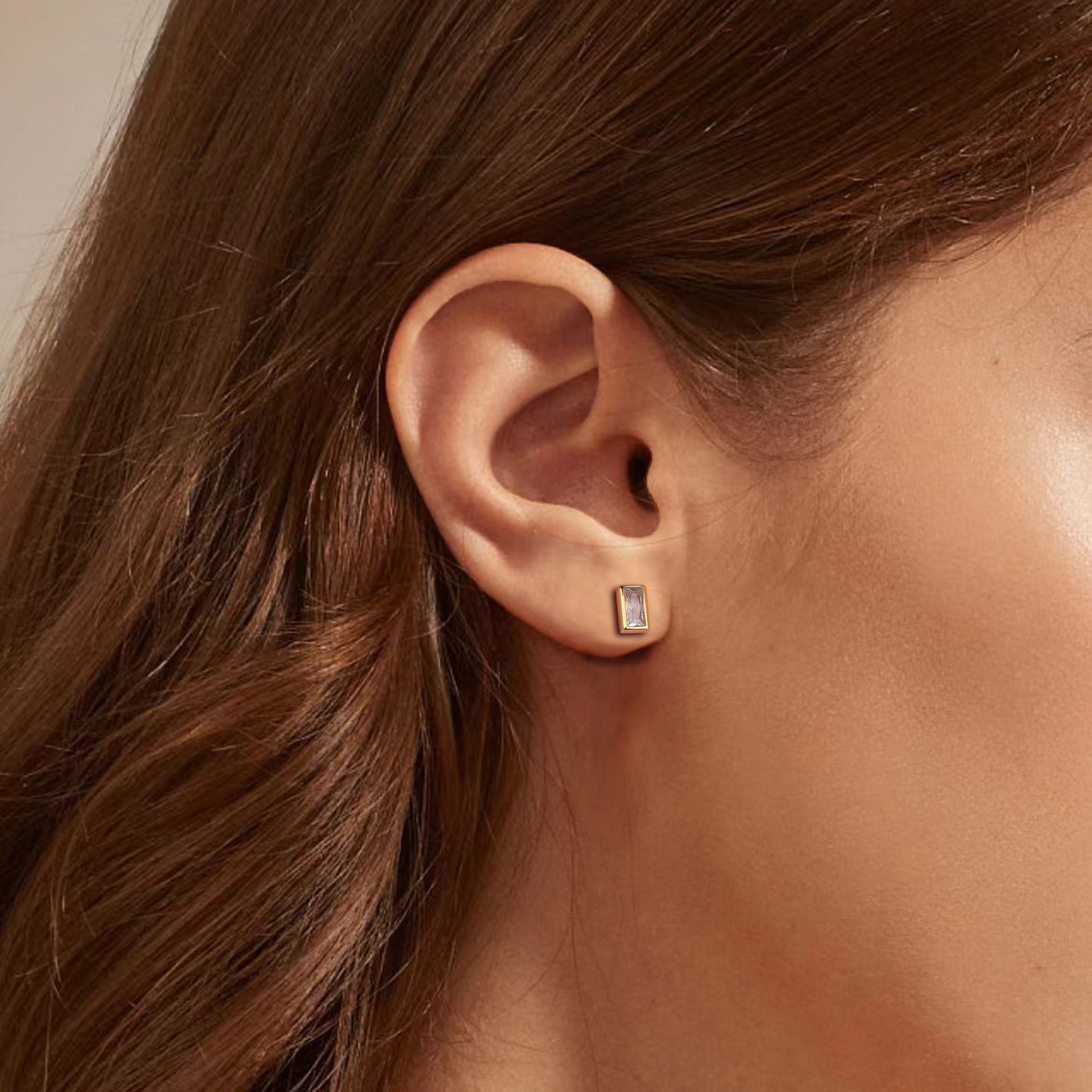 Close-up of an ear wearing a diamond stud earring with hair partially obscuring the view.