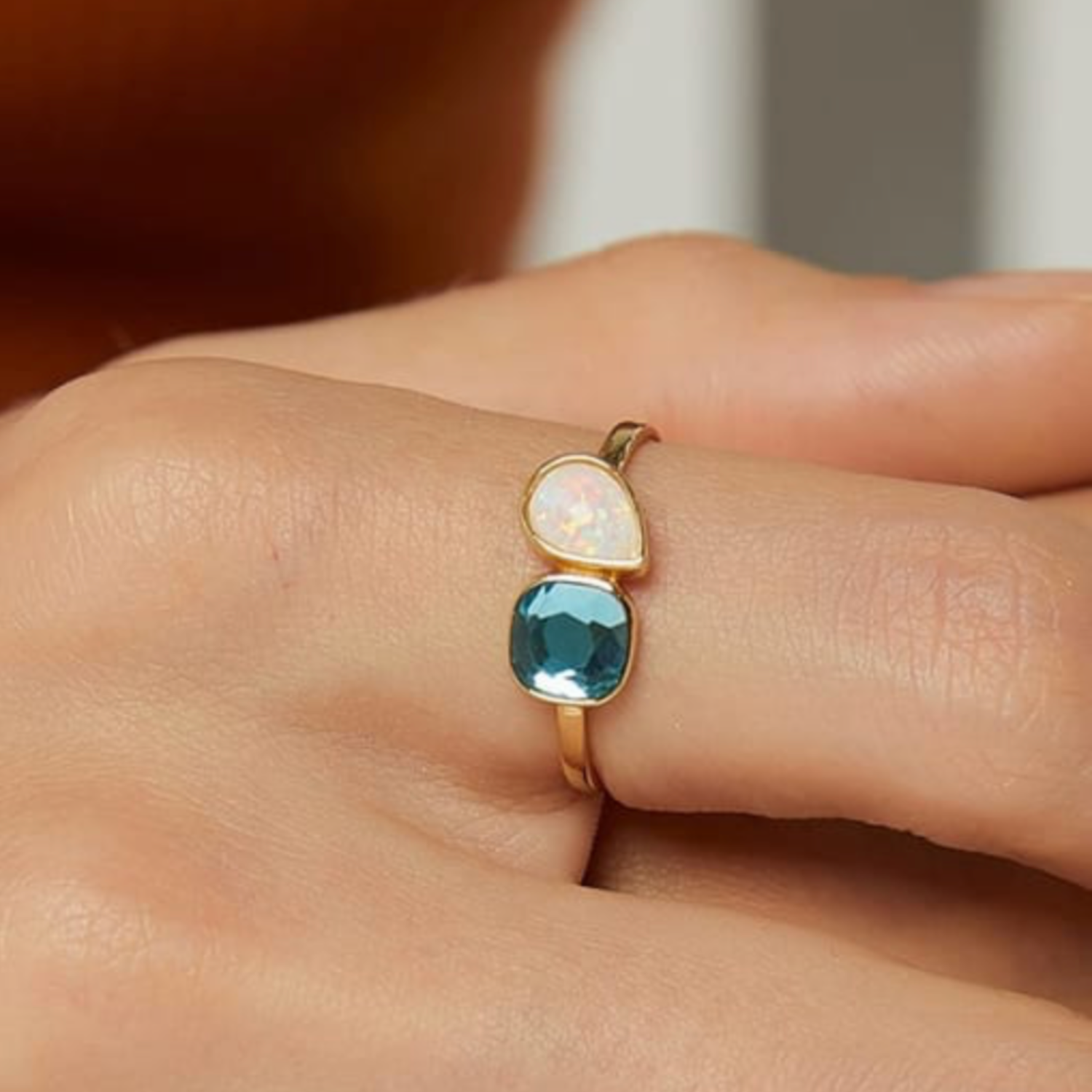 Gold ring with two gemstones on a person's finger