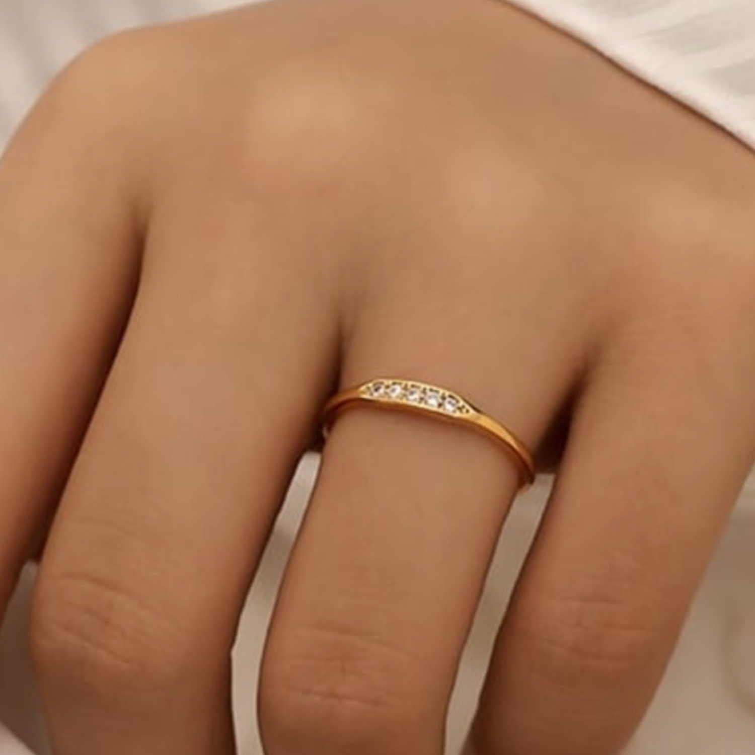 Gold ring with small CZ on a person's finger against a neutral background
