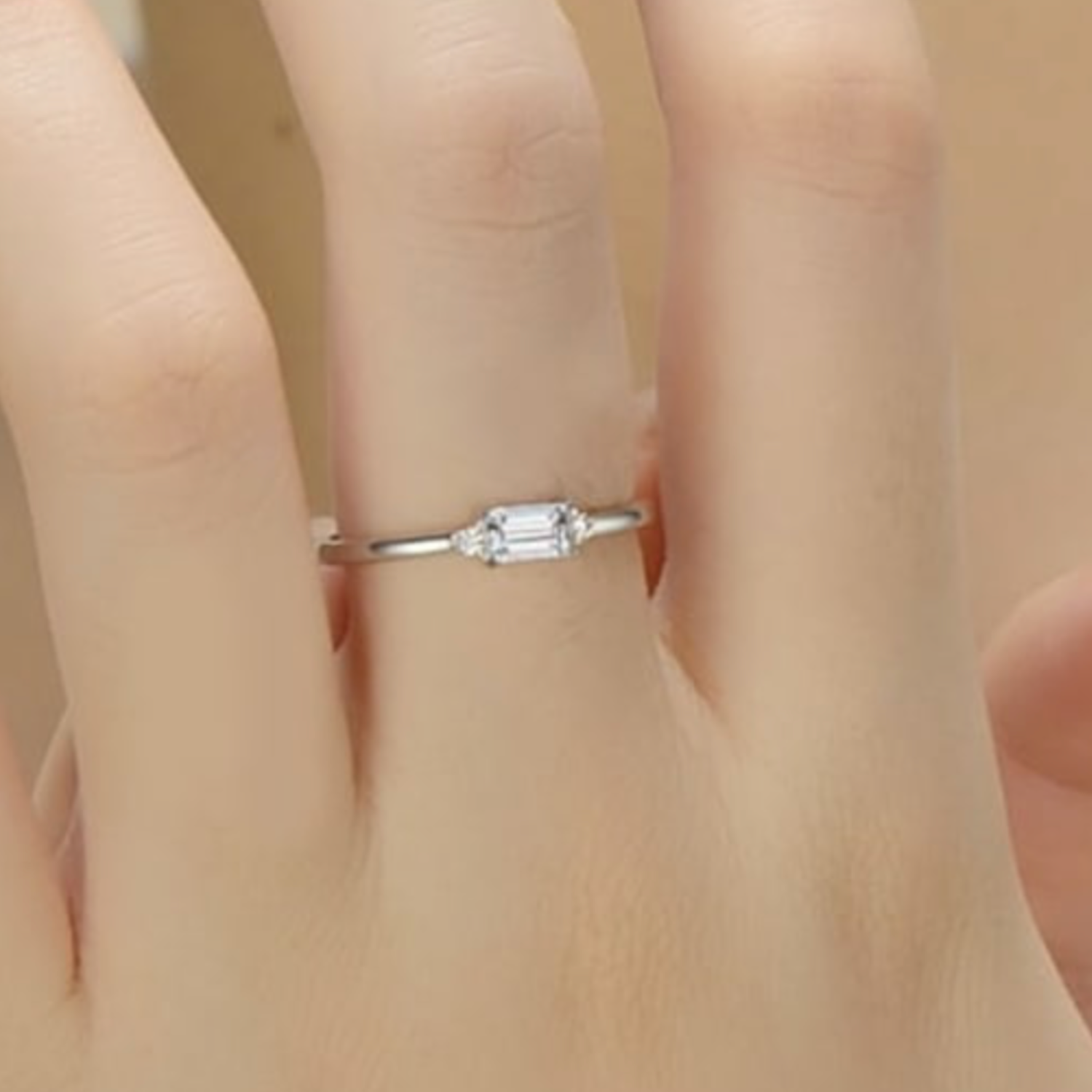 Silver ring with a CZ on a person's finger against a neutral background