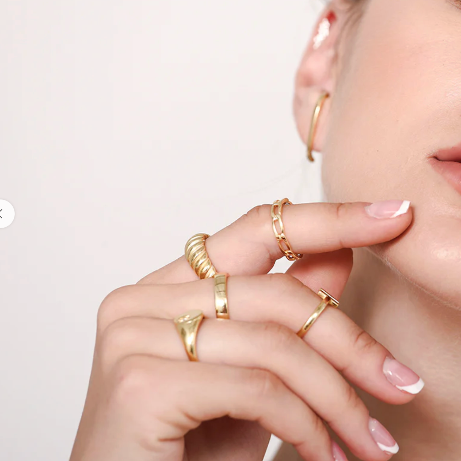 Close-up of a hand wearing multiple gold rings on a neutral background