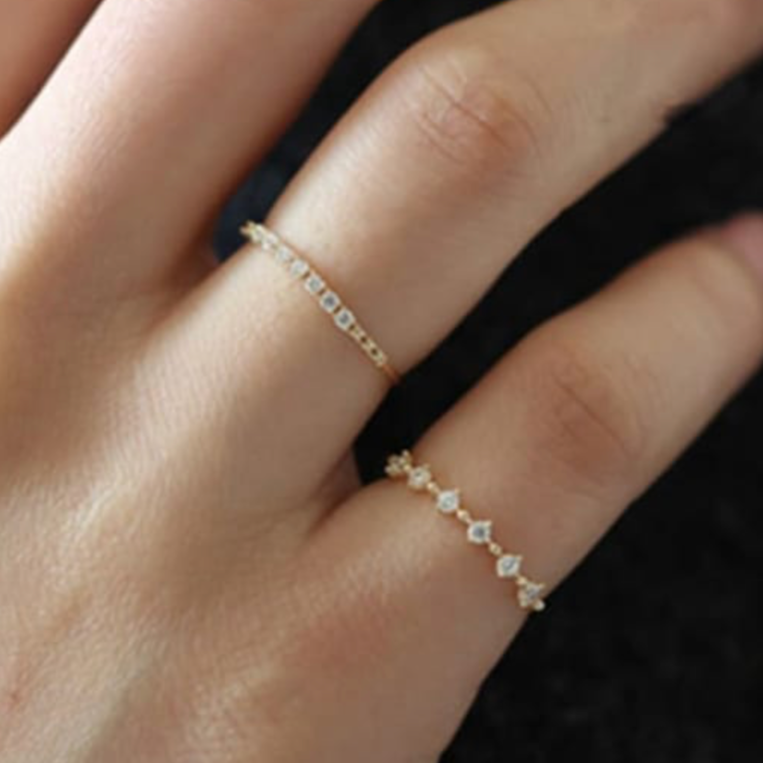 Close-up of a hand wearing two gold rings with small cubic zirconia on a dark background