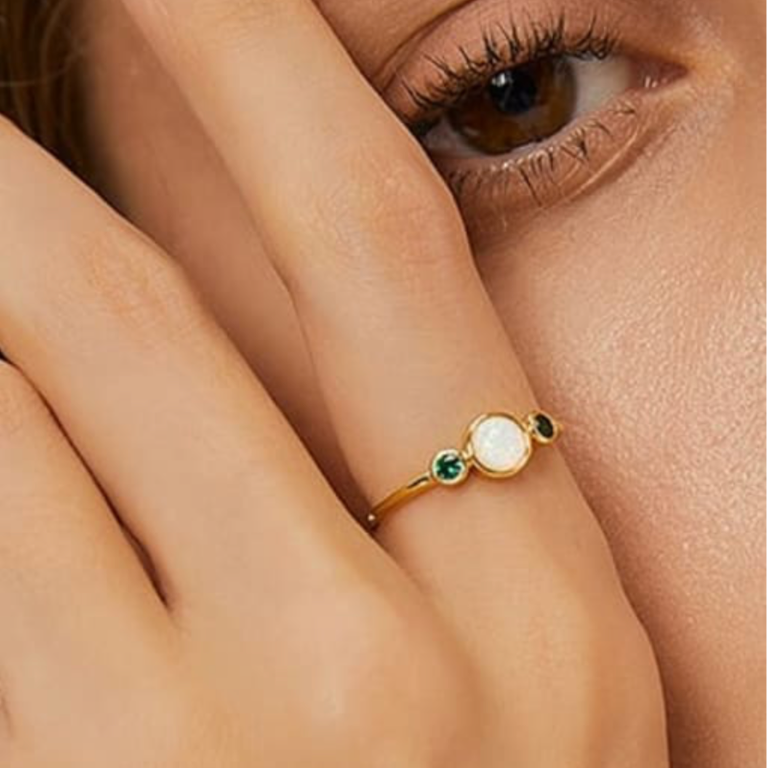 Gold ring with green gemstones on a person's finger