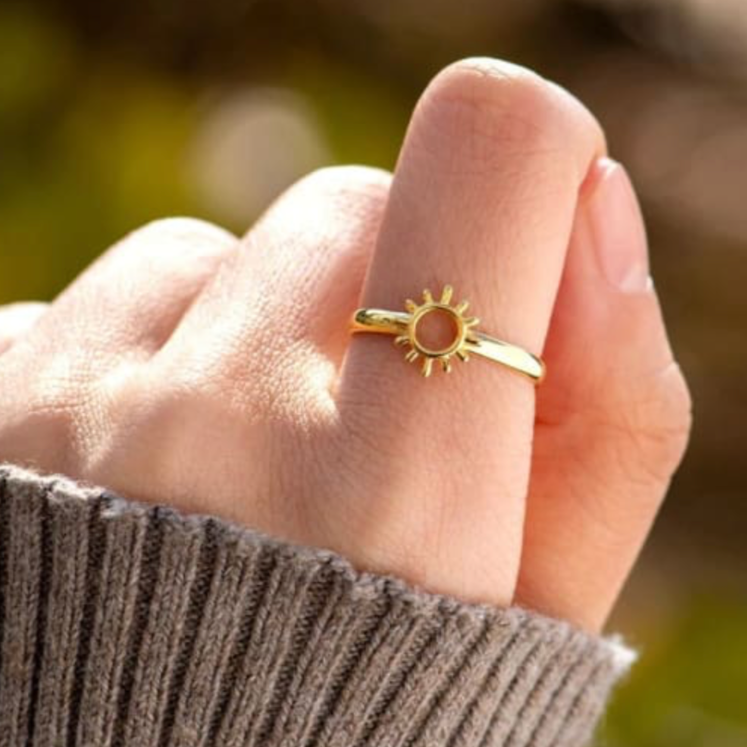 Gold sun-shaped ring on a person's finger with a blurred natural background