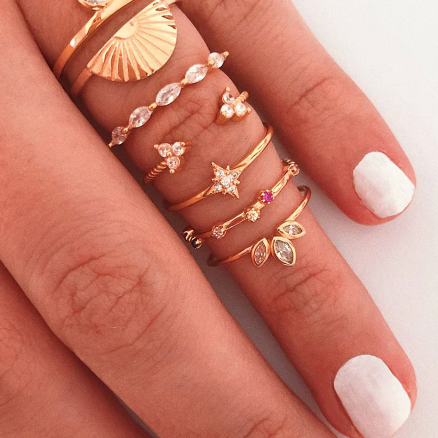 Hand wearing multiple gold rings with various designs on a light background