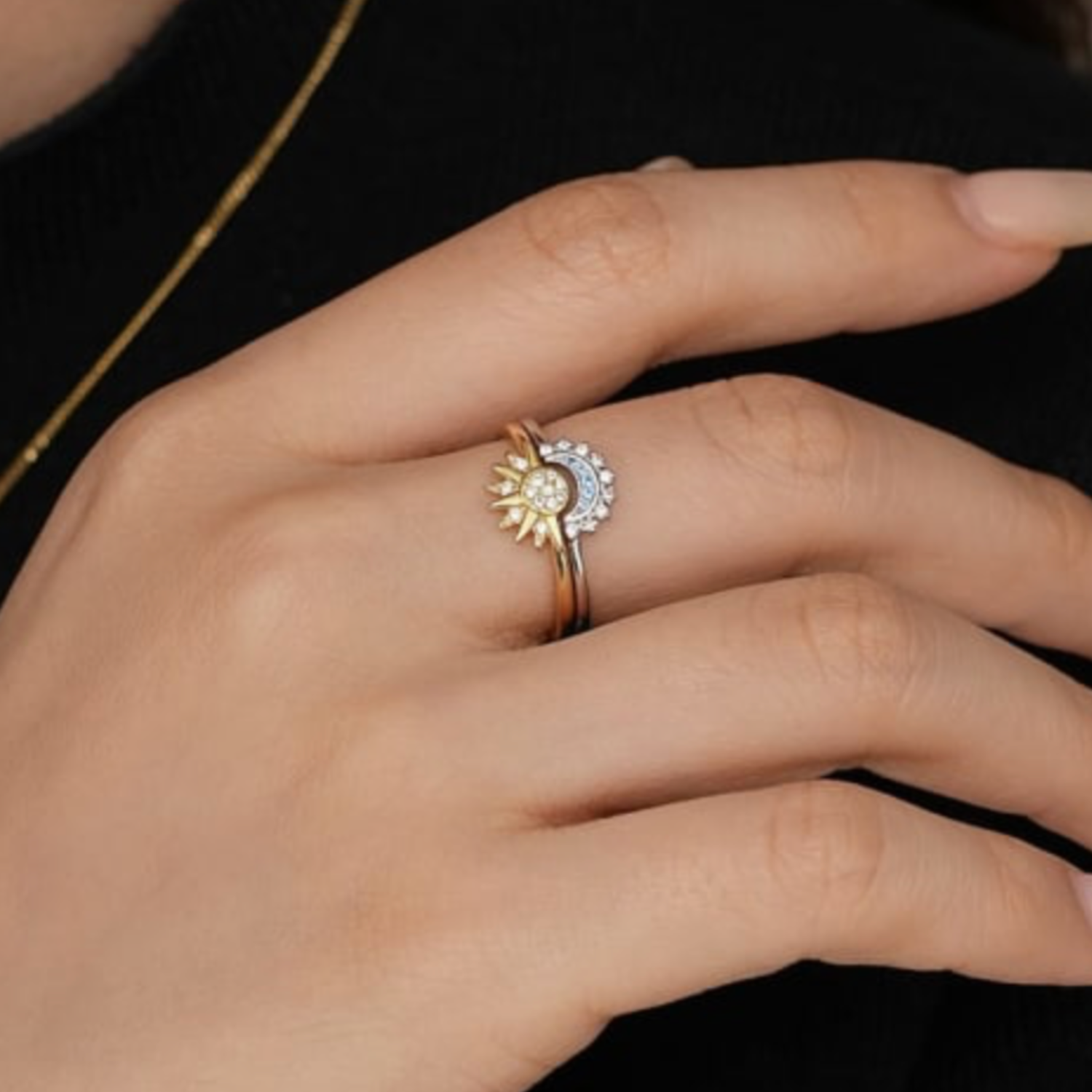 Hand wearing a gold ring with a sun design on a black background