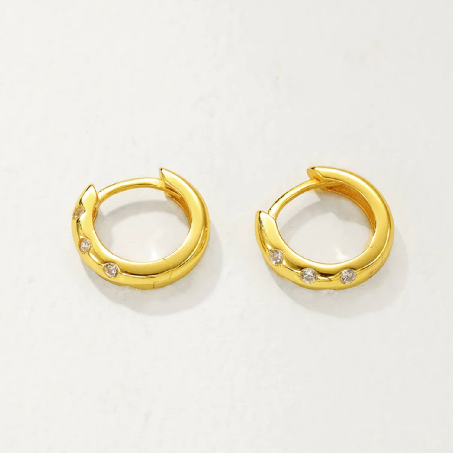 Gold hoop earrings with small diamonds on a light gray background