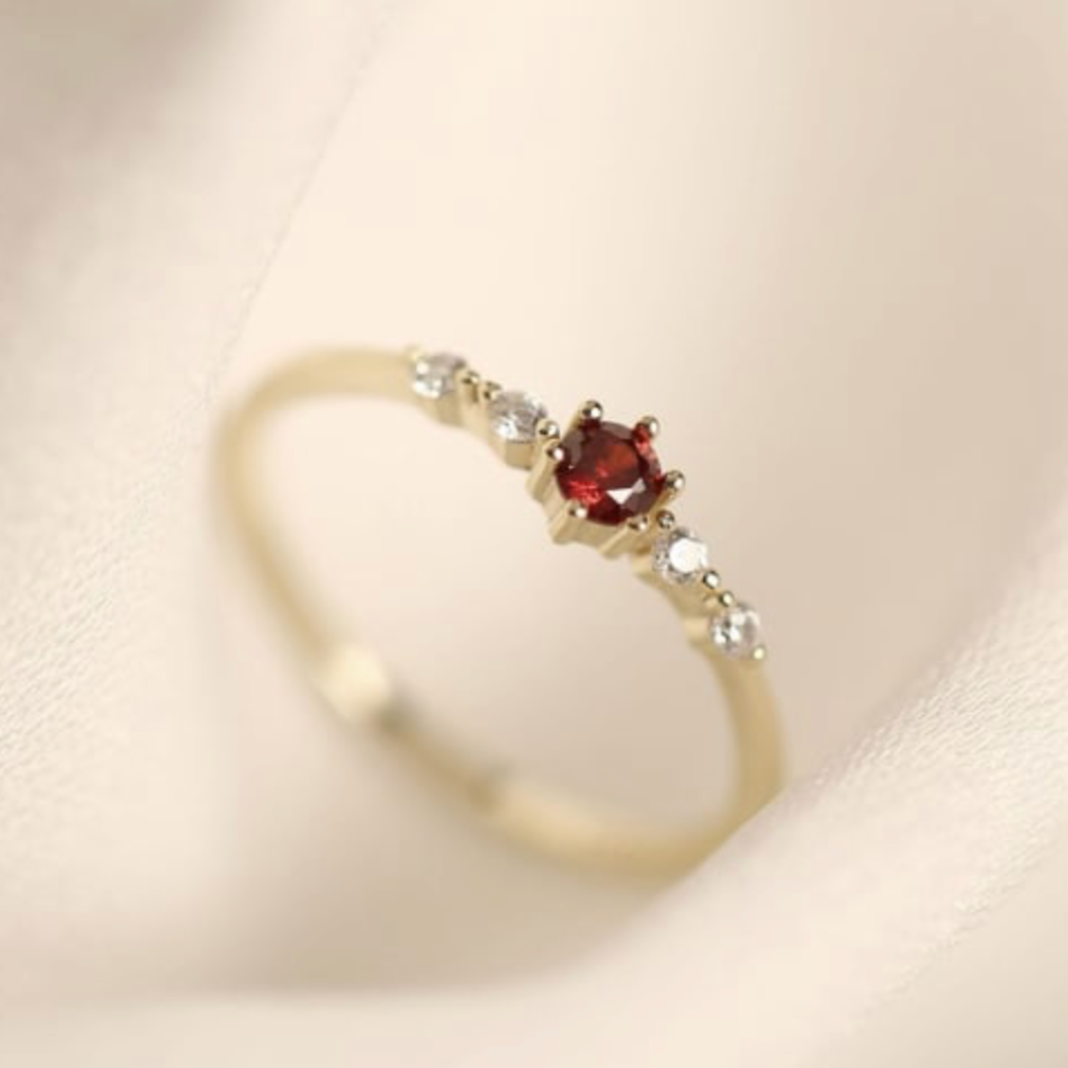 Gold ring with a red gemstone and smaller clear stones on a beige background