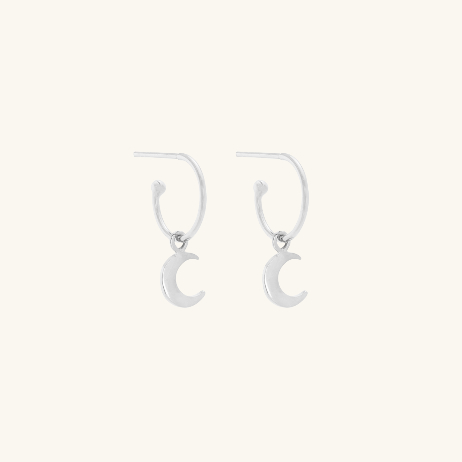 Silver crescent moon earrings on a cream background