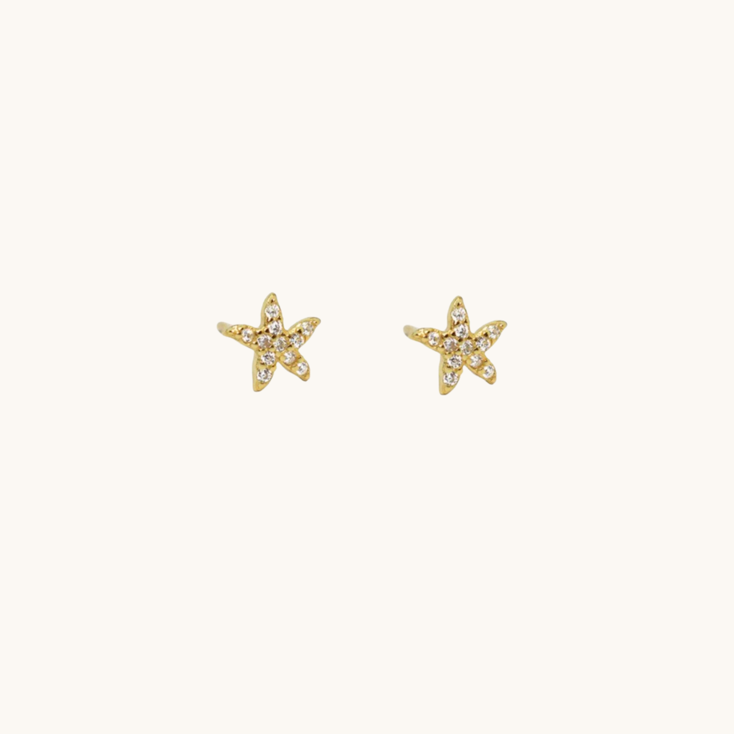 A pair of gold starfish stud earrings with small clear stones, displayed on a clean off-white background.