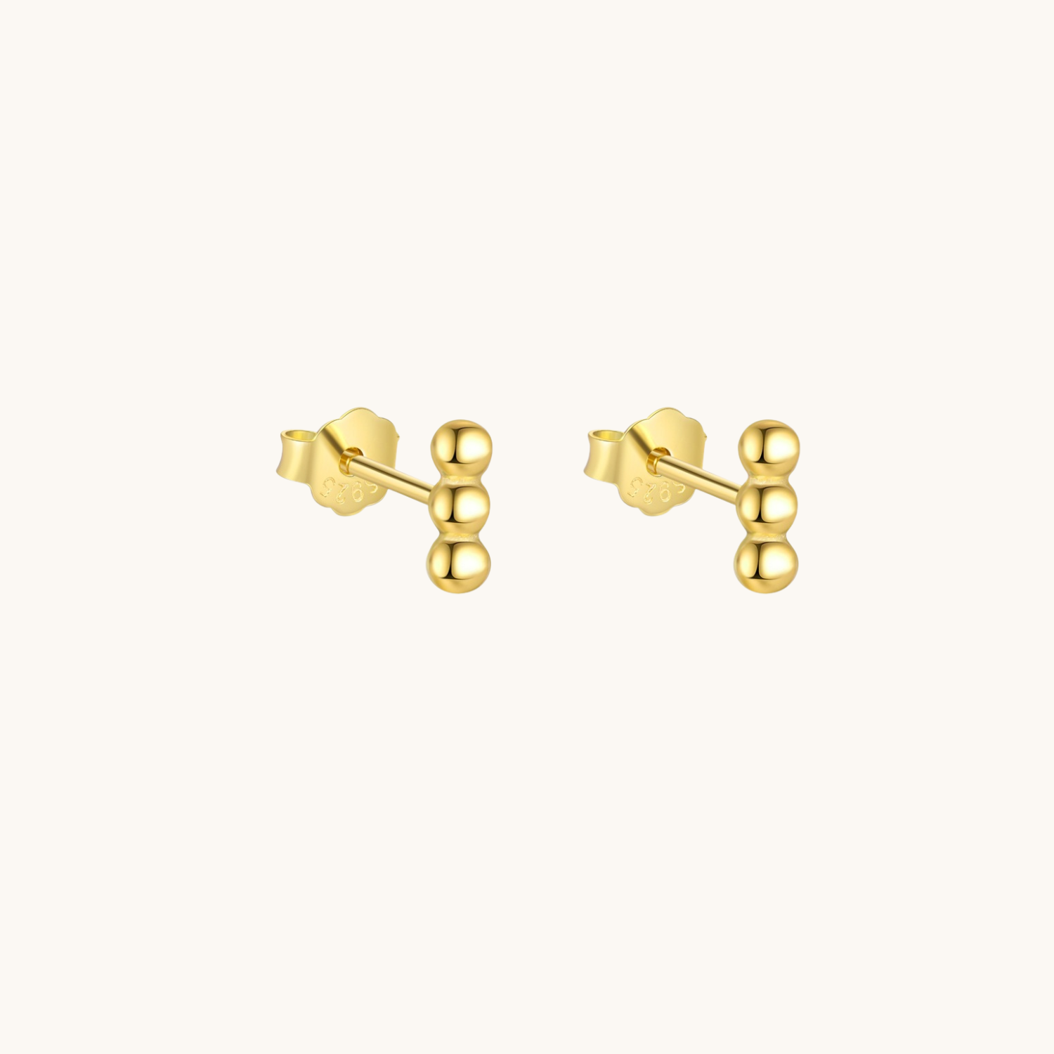 A pair of gold stud earrings with a cluster of three polished spherical beads on a straight post, shown against a solid off-white background.