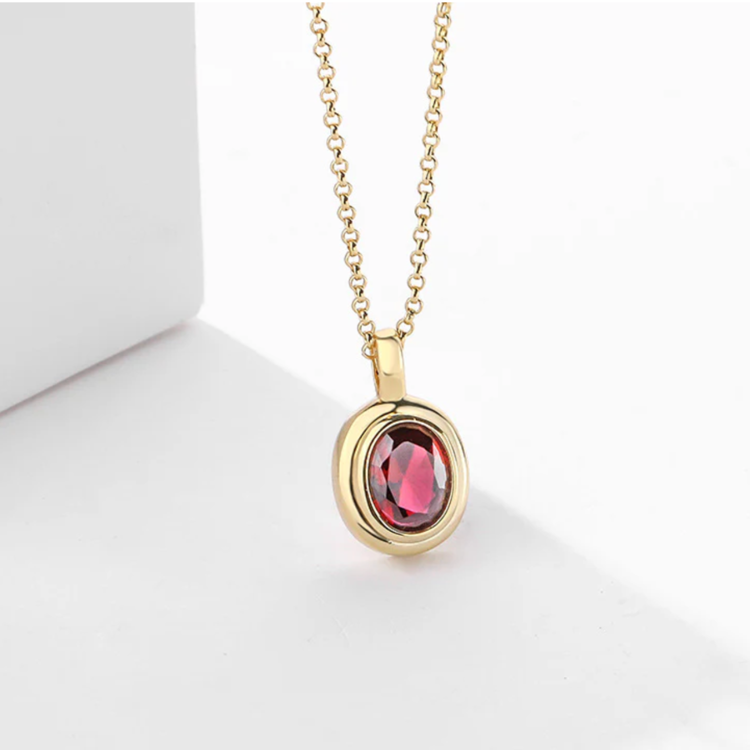 Gold necklace with a red gemstone pendant on a white background