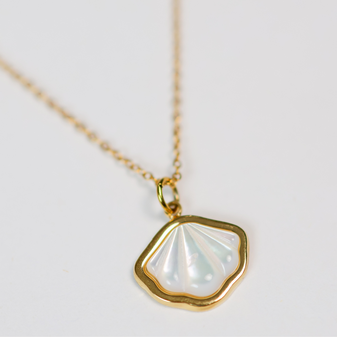 Gold necklace with a shell-shaped pendant on a light gray background