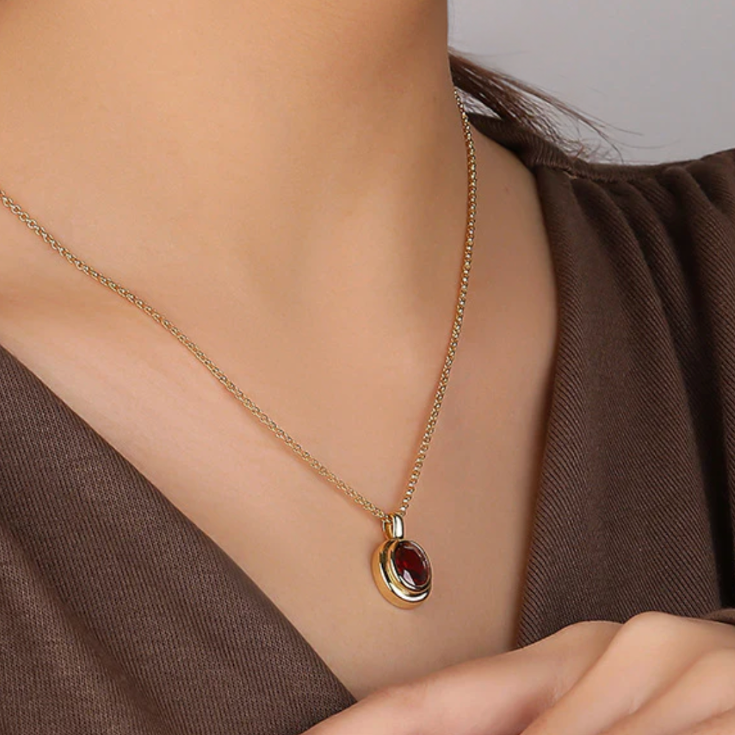 Gold necklace with a red gemstone pendant on a model wearing a brown top.