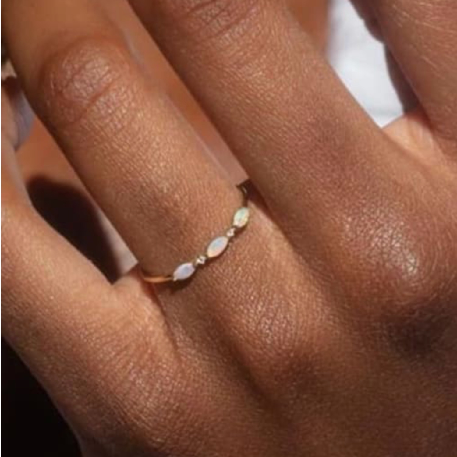 Close-up of a hand wearing a delicate ring with opal stones on a neutral background