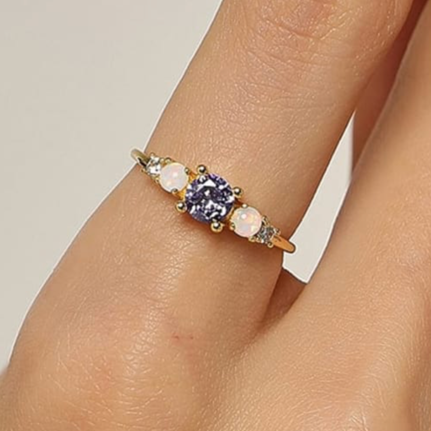 Gold ring with a purple gemstone on a person's finger against a neutral background